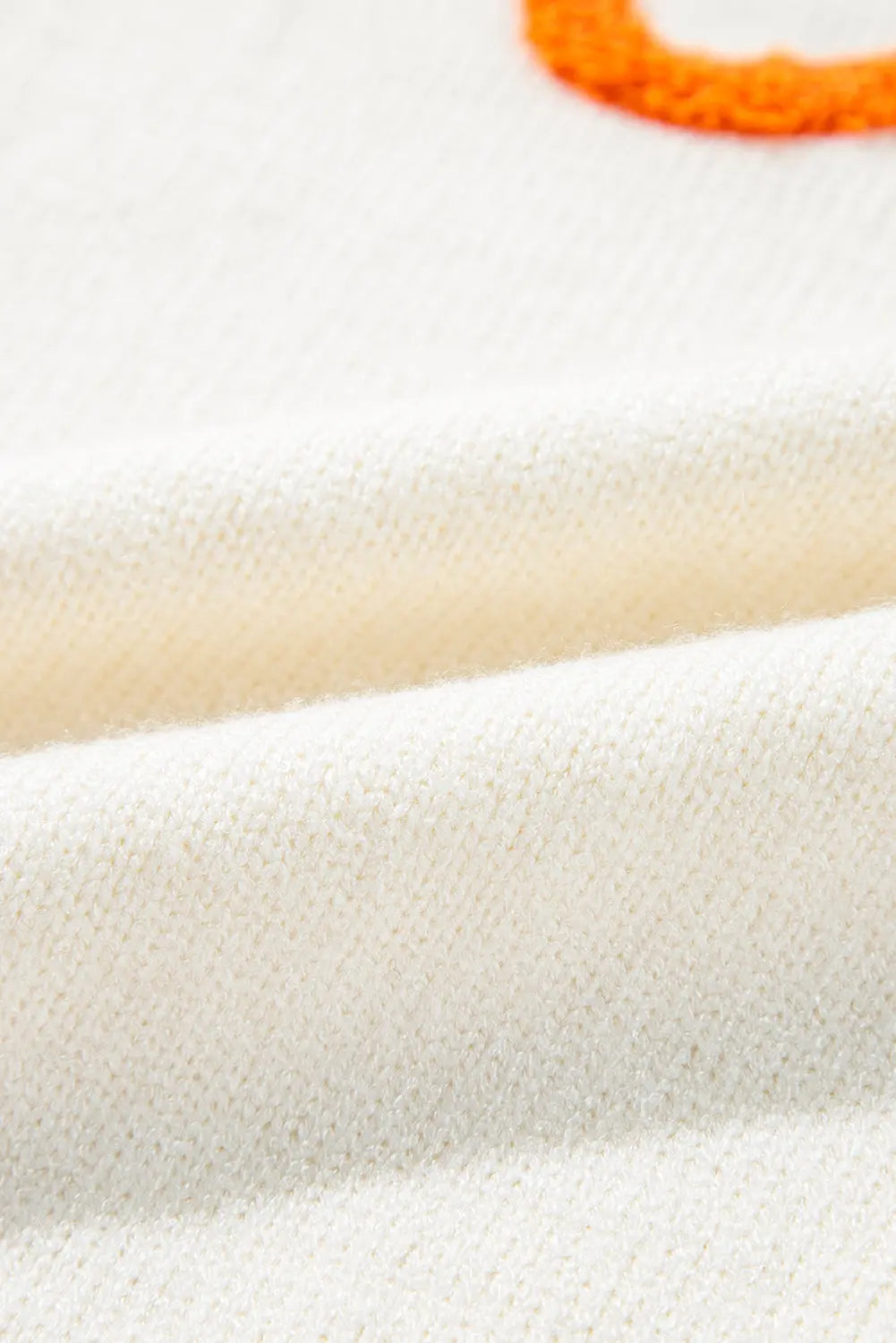 Close-up of cream knit fabric with soft folds and small orange accent.