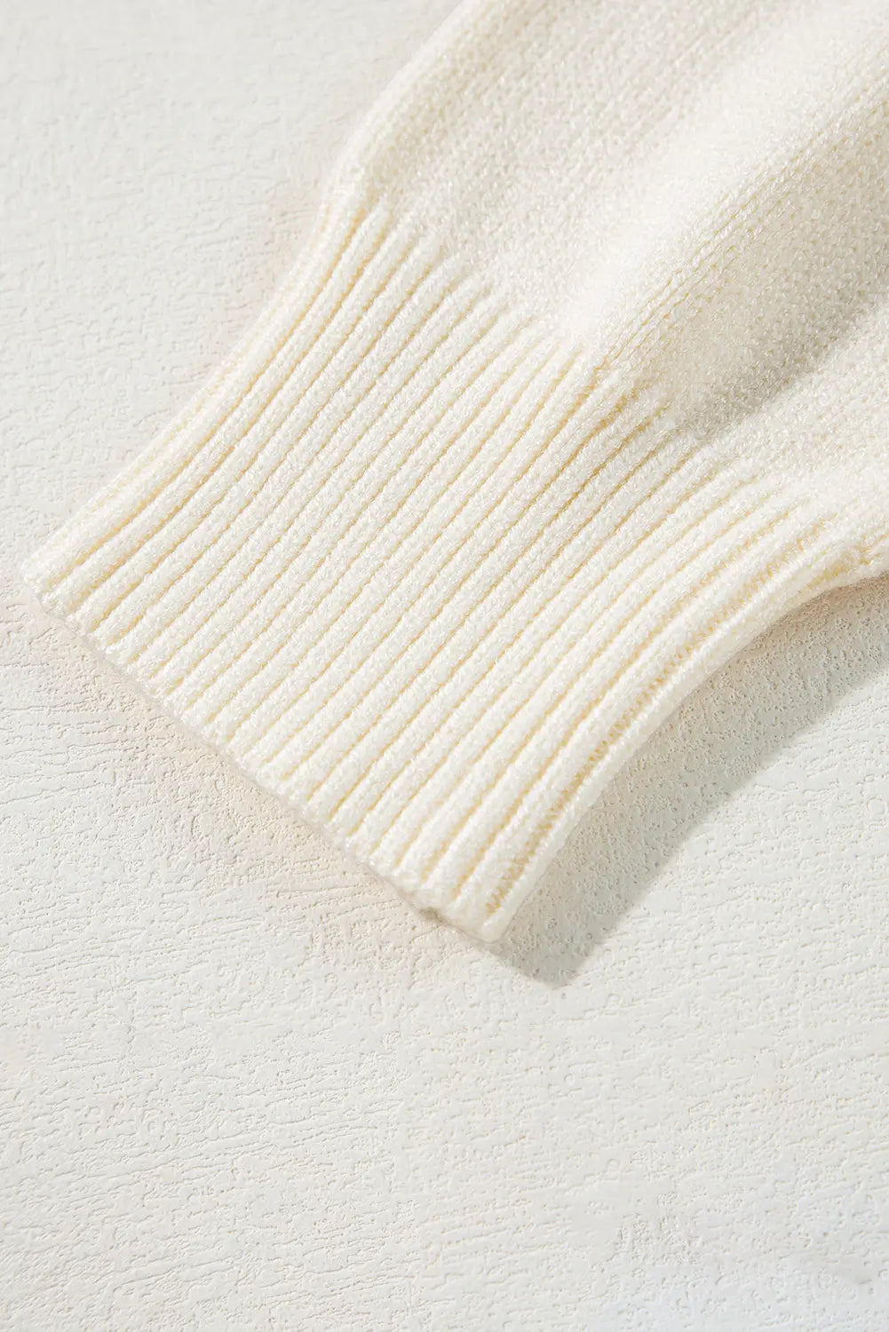 Close-up of cream ribbed knit cuff with textured stitching detail.
