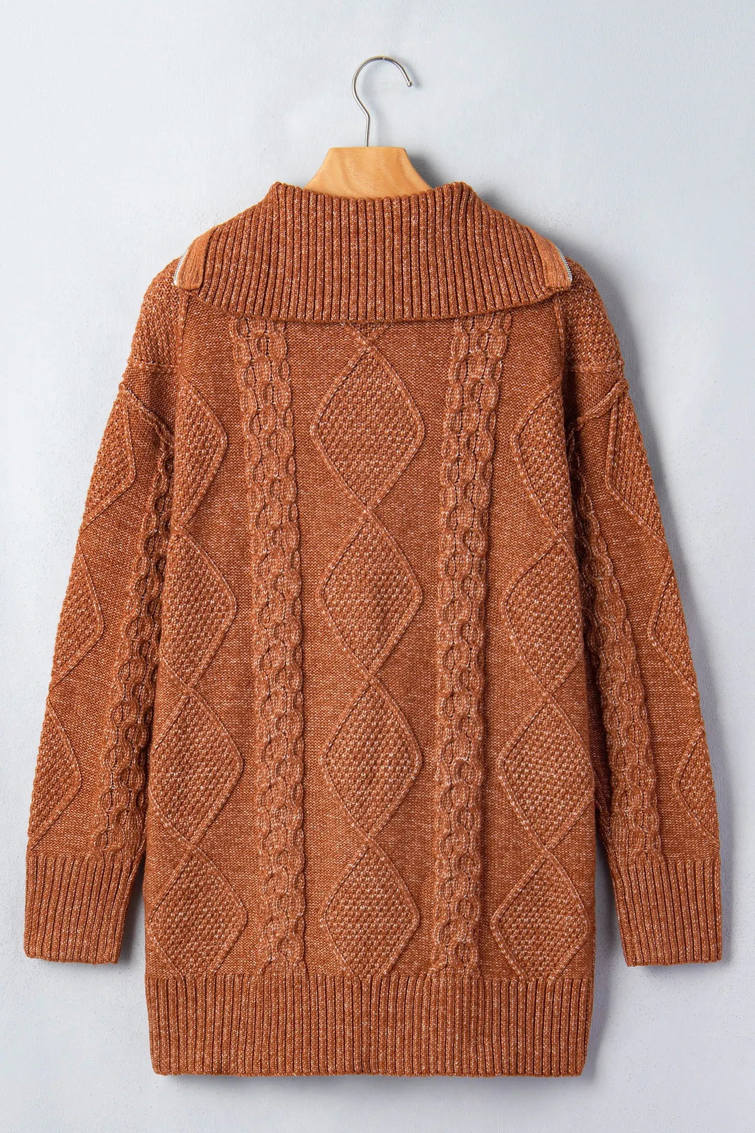 Rust-brown diamond cable-knit sweater with mock neck hanging on wooden hanger against light gray.