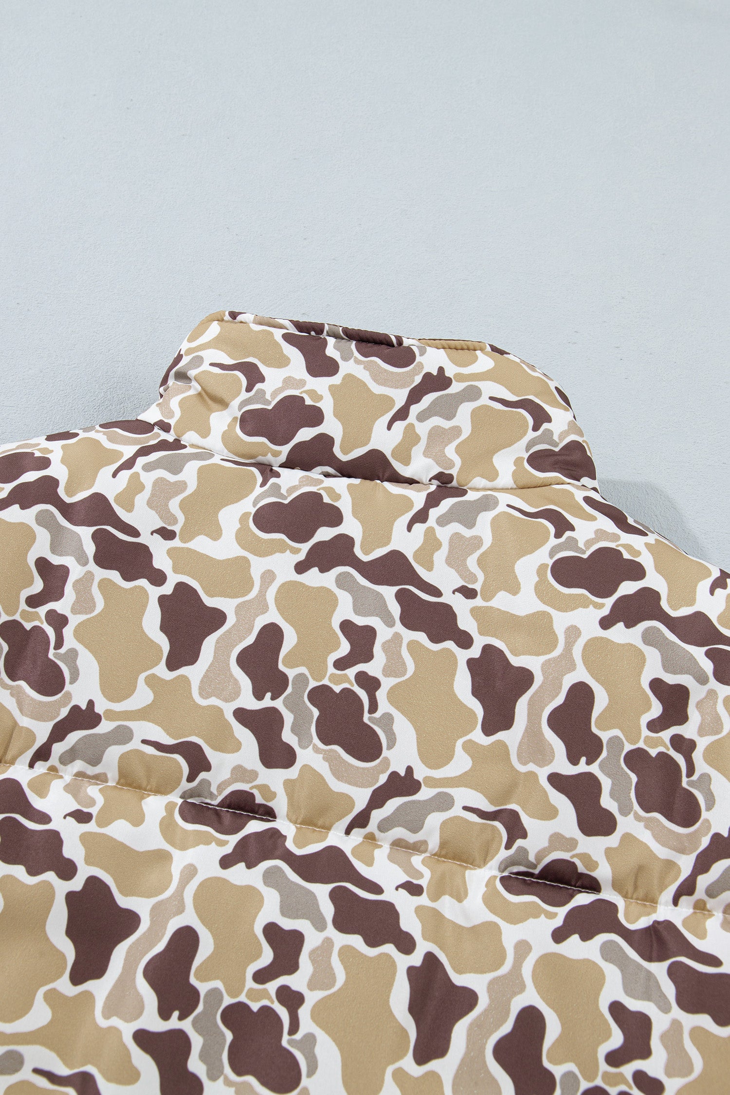 Close-up of brown, beige, and white camouflage puffer jacket with quilted texture against light gray.