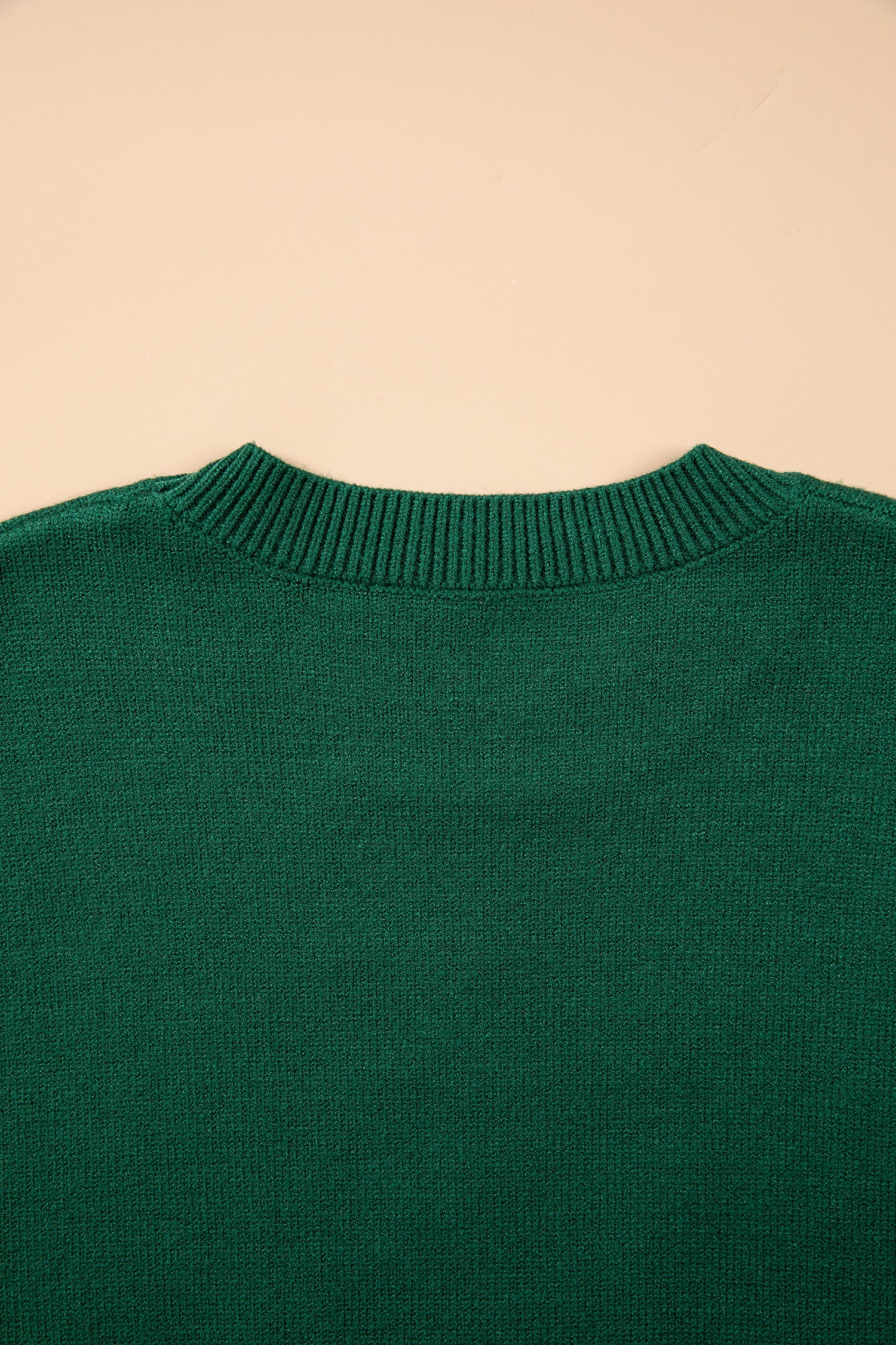 Close-up of the back of a dark green knit sweater with a ribbed crew neck, set against a solid beige background.