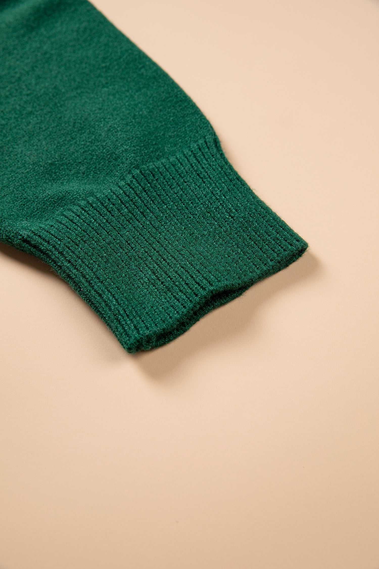 A close-up of a dark green ribbed knit sleeve or cuff on a solid beige background.