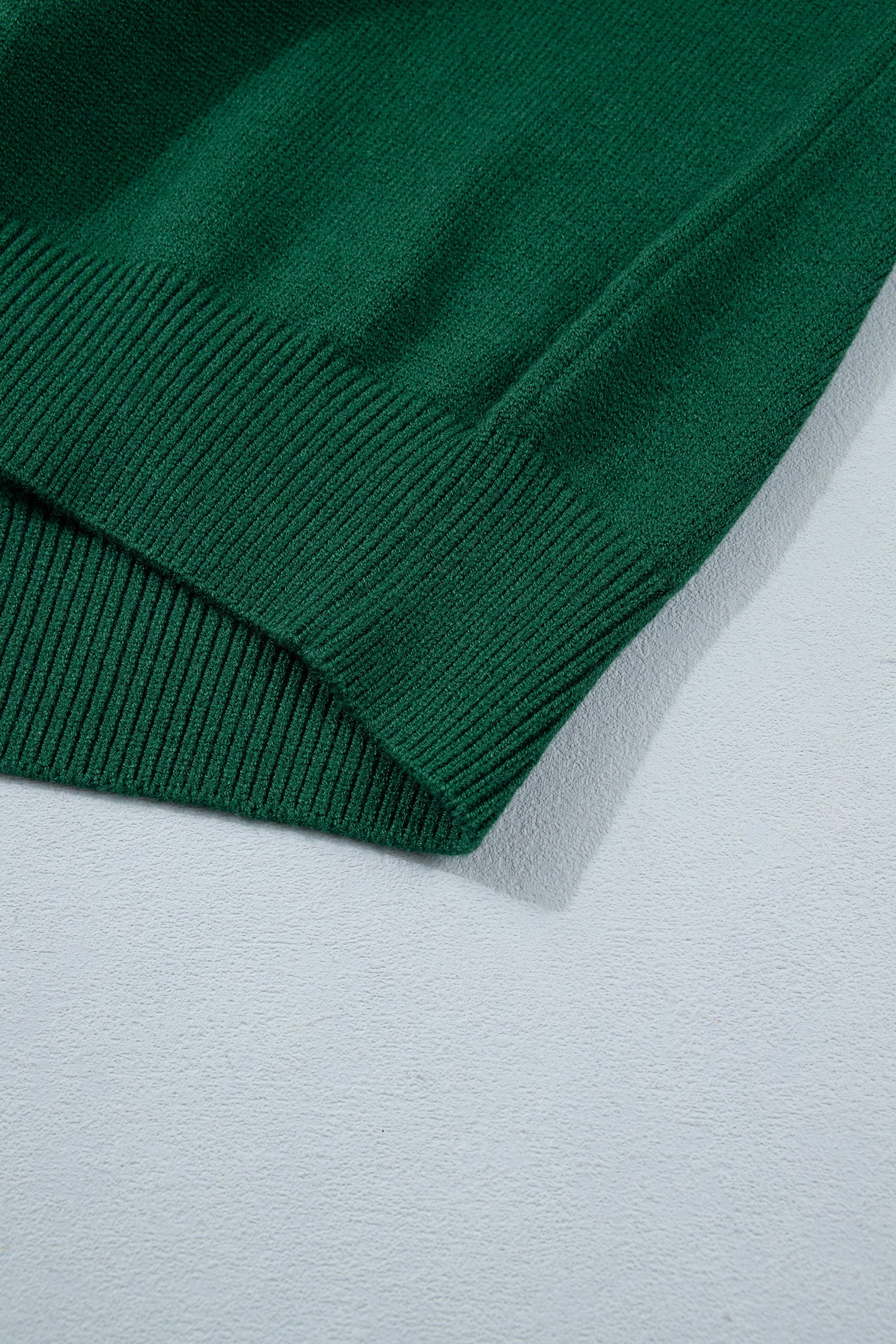 Close-up of dark green ribbed knit fabric corner on light gray surface.