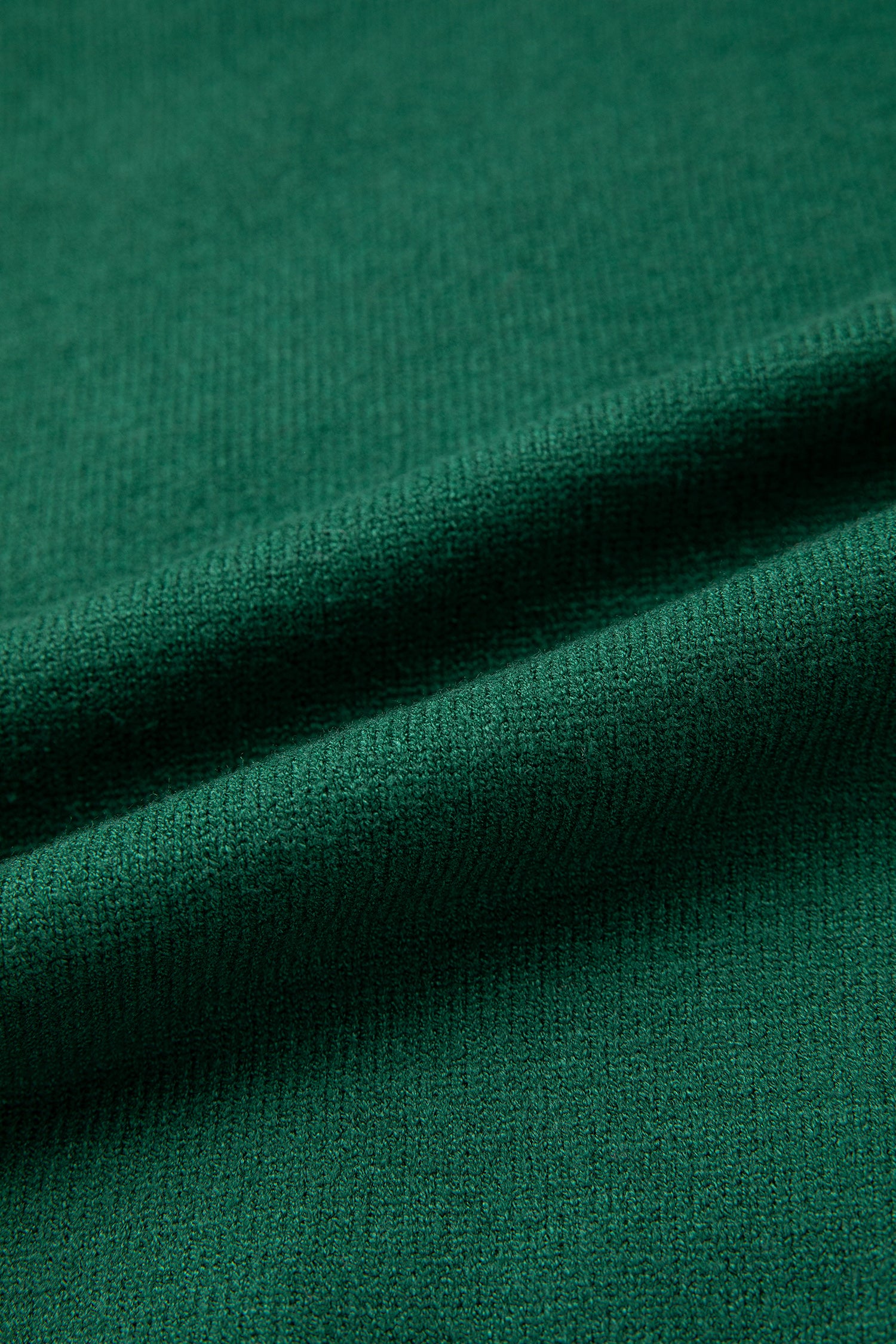 A close-up of dark green knit fabric with soft folds showing the texture and color.