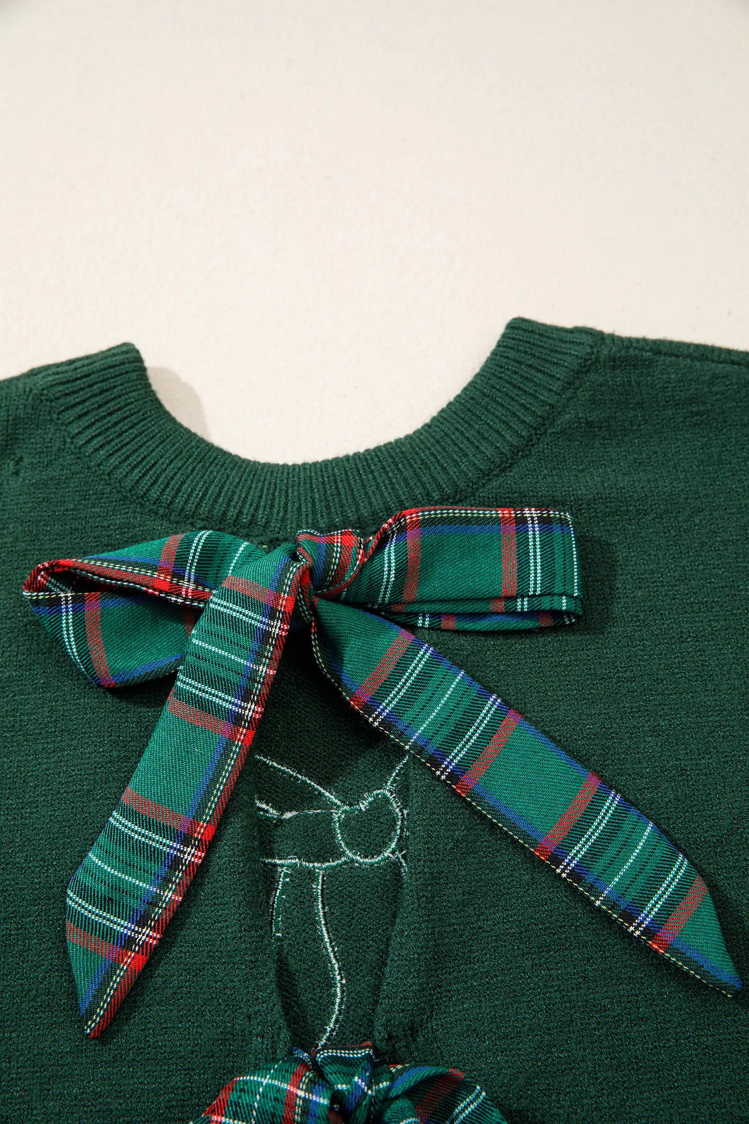 Close-up of dark green sweater with large green plaid bows at neck and hem.
