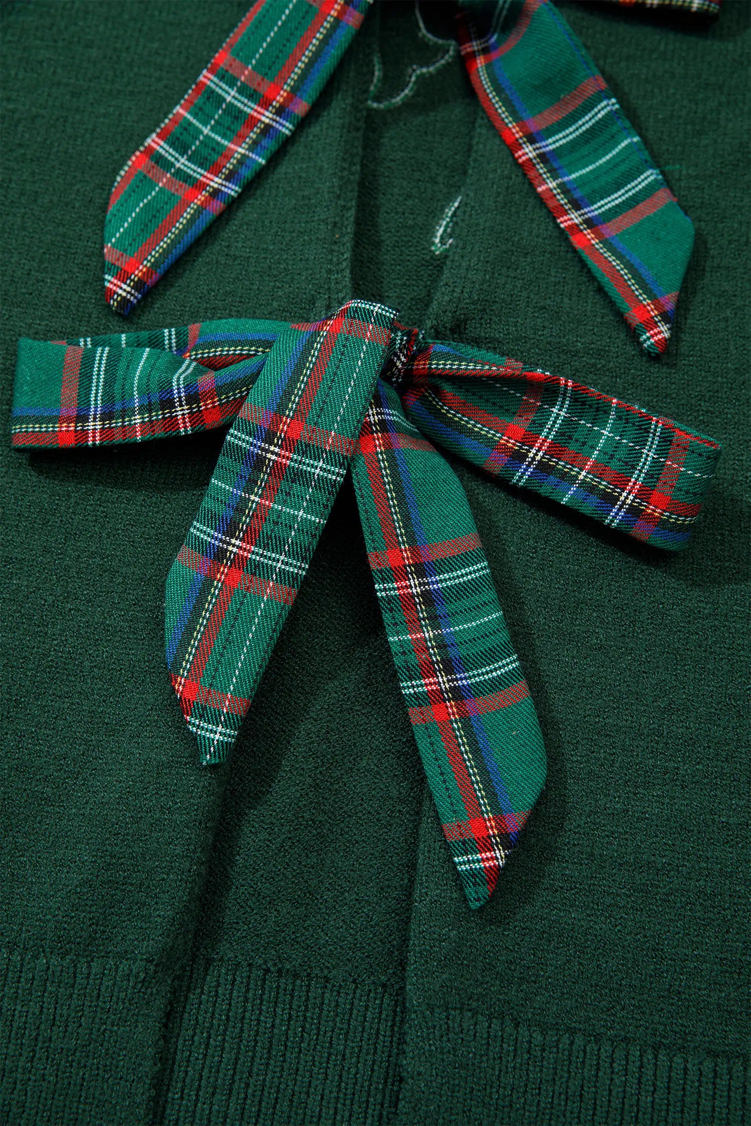 Close-up of dark green sweater with large green-red-white-blue tartan bow at chest.