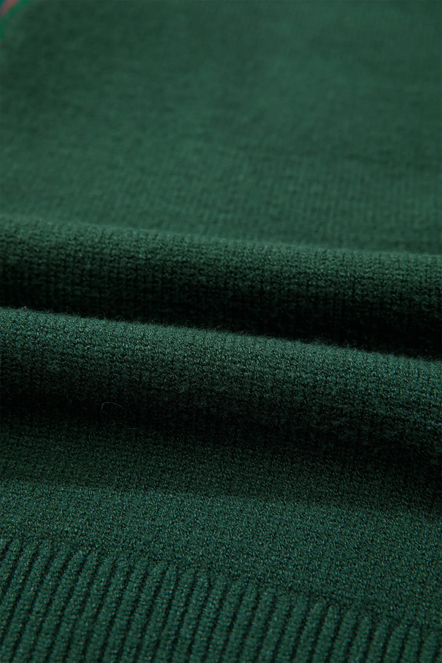 A close-up of dark forest green knit fabric with a ribbed texture and soft folds.