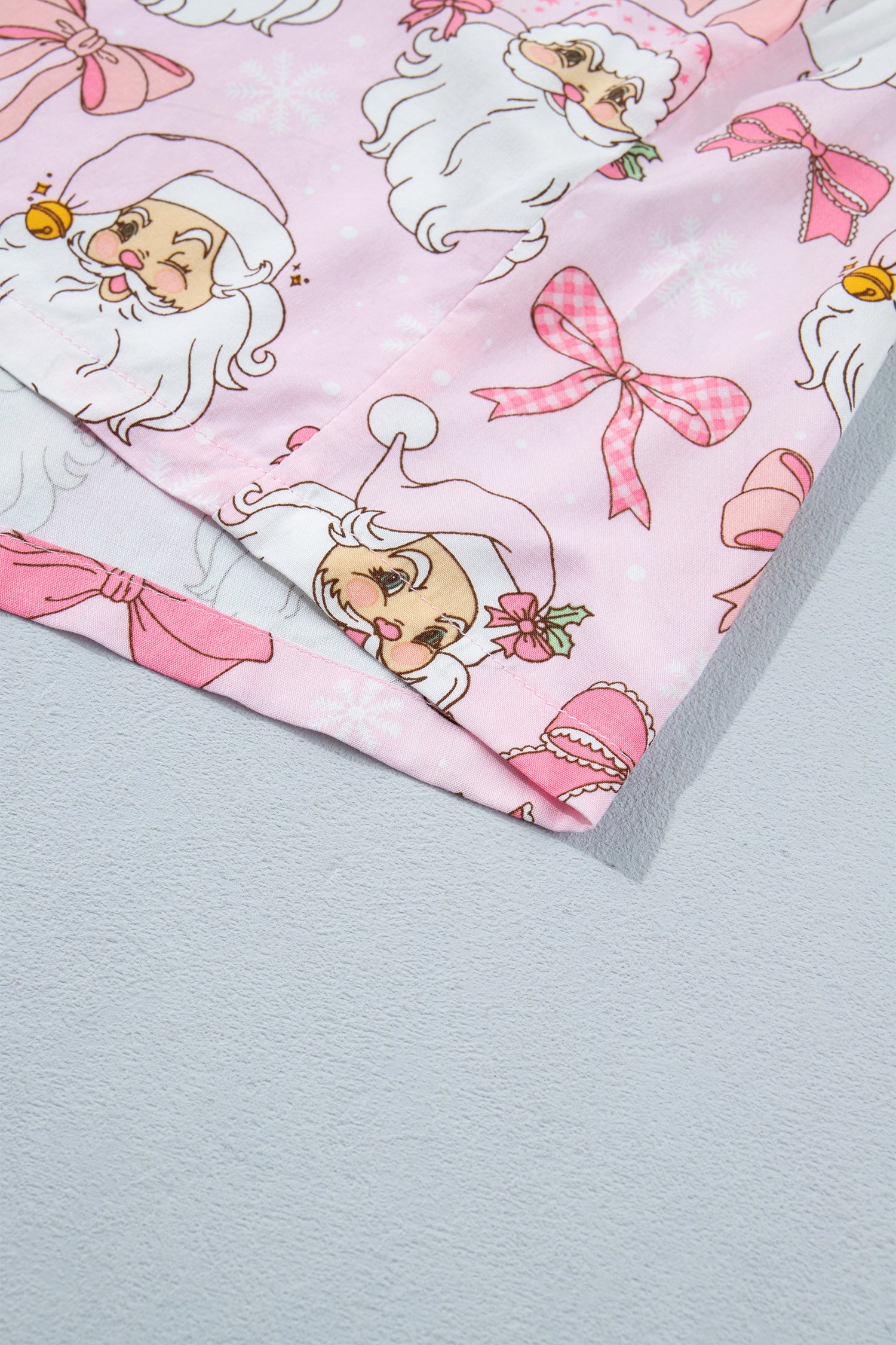 Folded light pink fabric with cartoon Santa and pink bow print.