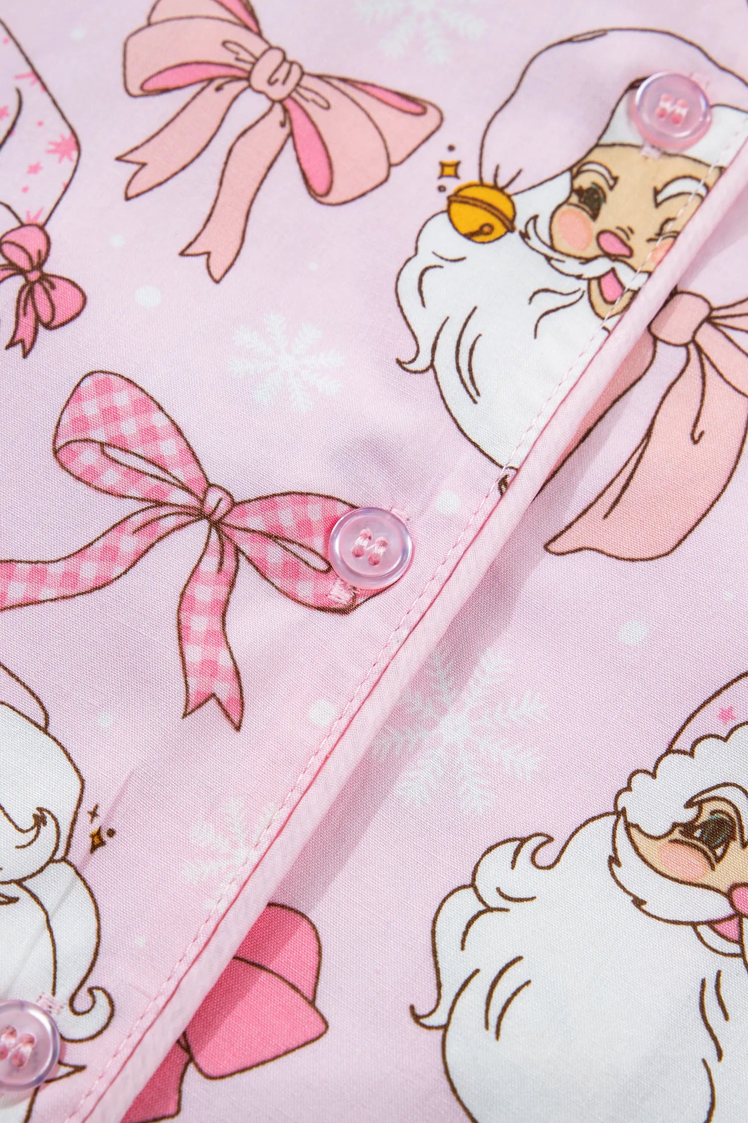 Close-up of light pink fabric with Santa, bows, snowflakes, and snap buttons.