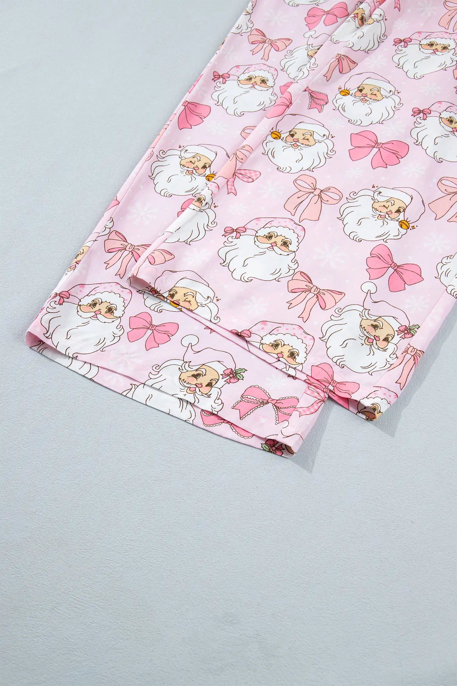 Pink pajama pants with an all-over cartoon Santa Claus and bow pattern, folded on a light gray surface.
