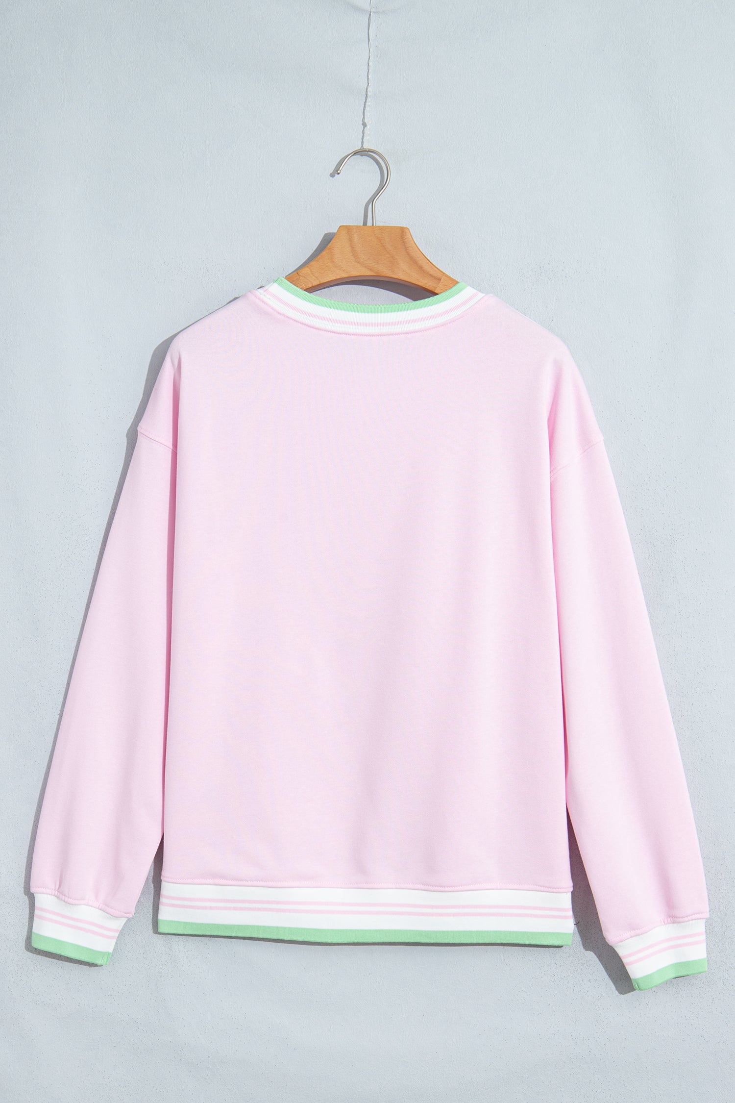 A light pink crewneck sweatshirt hanging on a wooden hanger against a light gray background