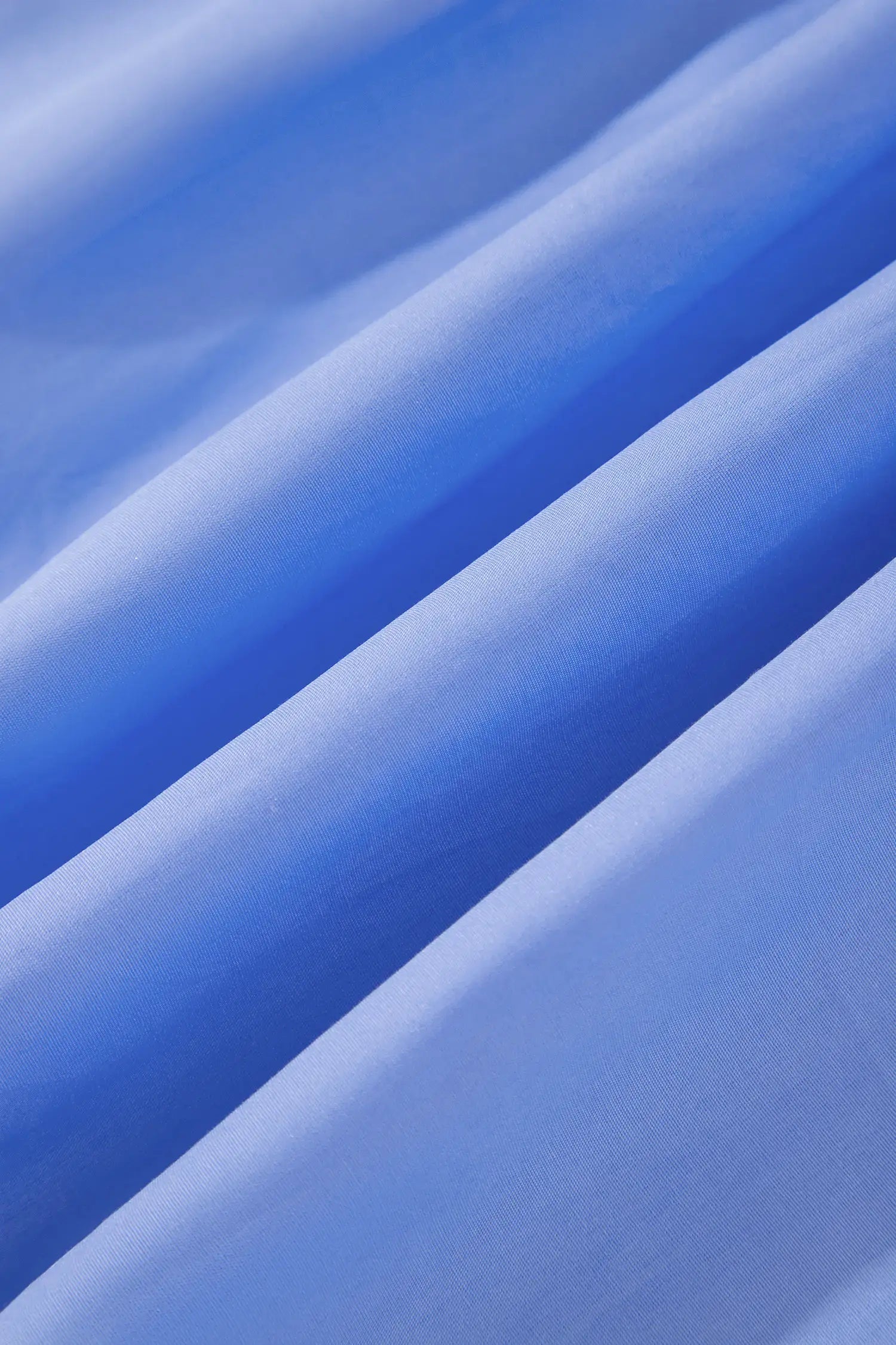 A close-up of draped blue fabric with soft diagonal folds and a smooth, slightly sheer texture.