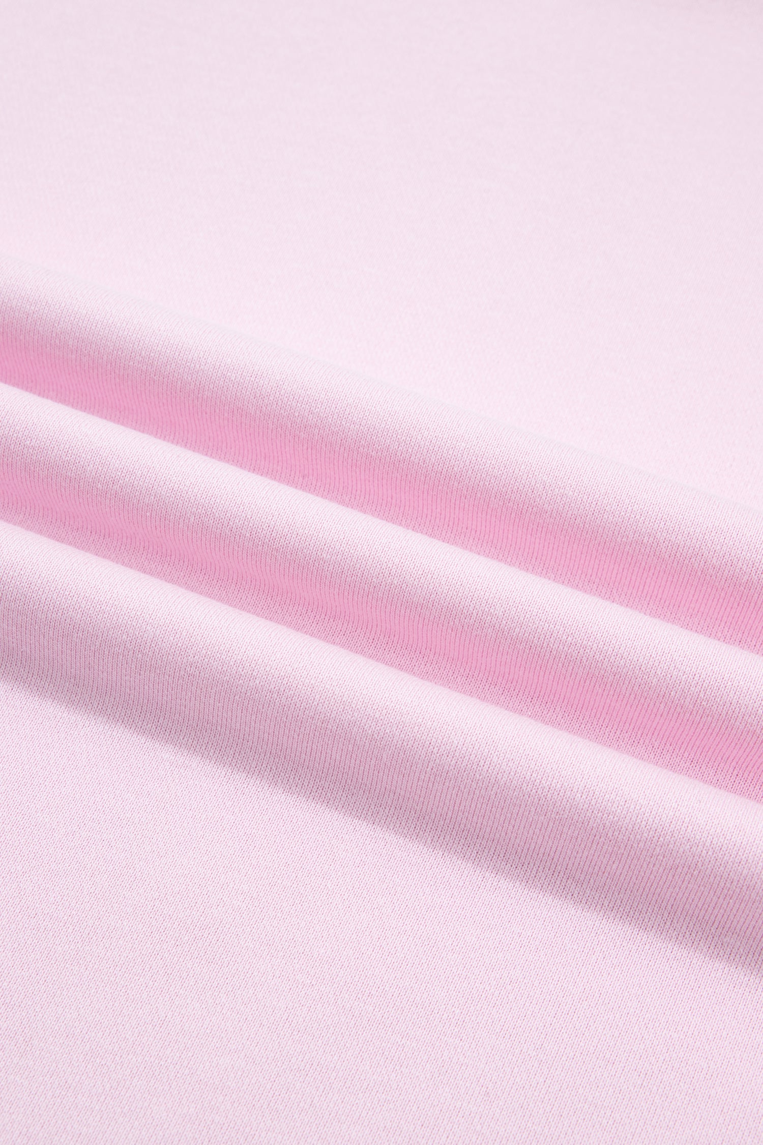 A close-up of light pink fabric with soft diagonal folds and a smooth texture.
