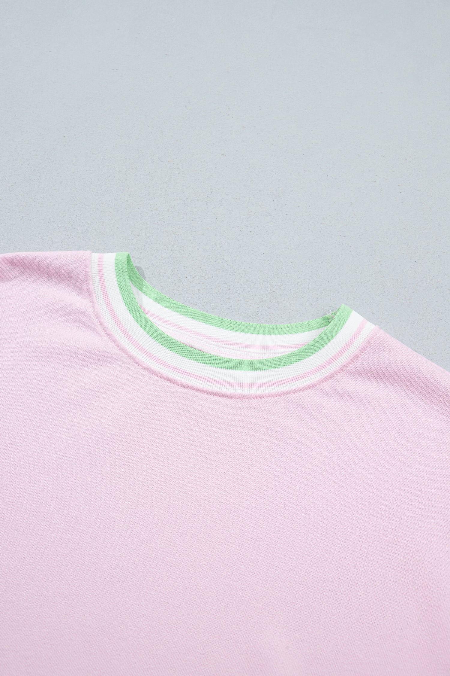 Close-up of a light pink crewneck shirt with a striped collar featuring mint green, white
