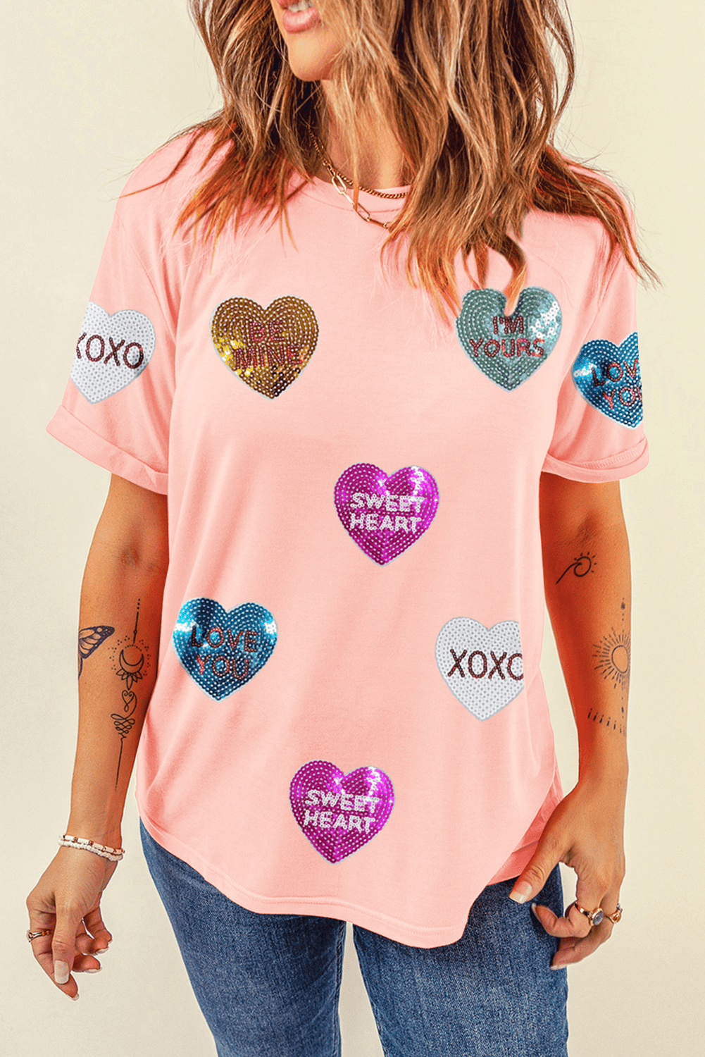 Person wearing a pink t-shirt with heart-shaped sequin designs on a beige background