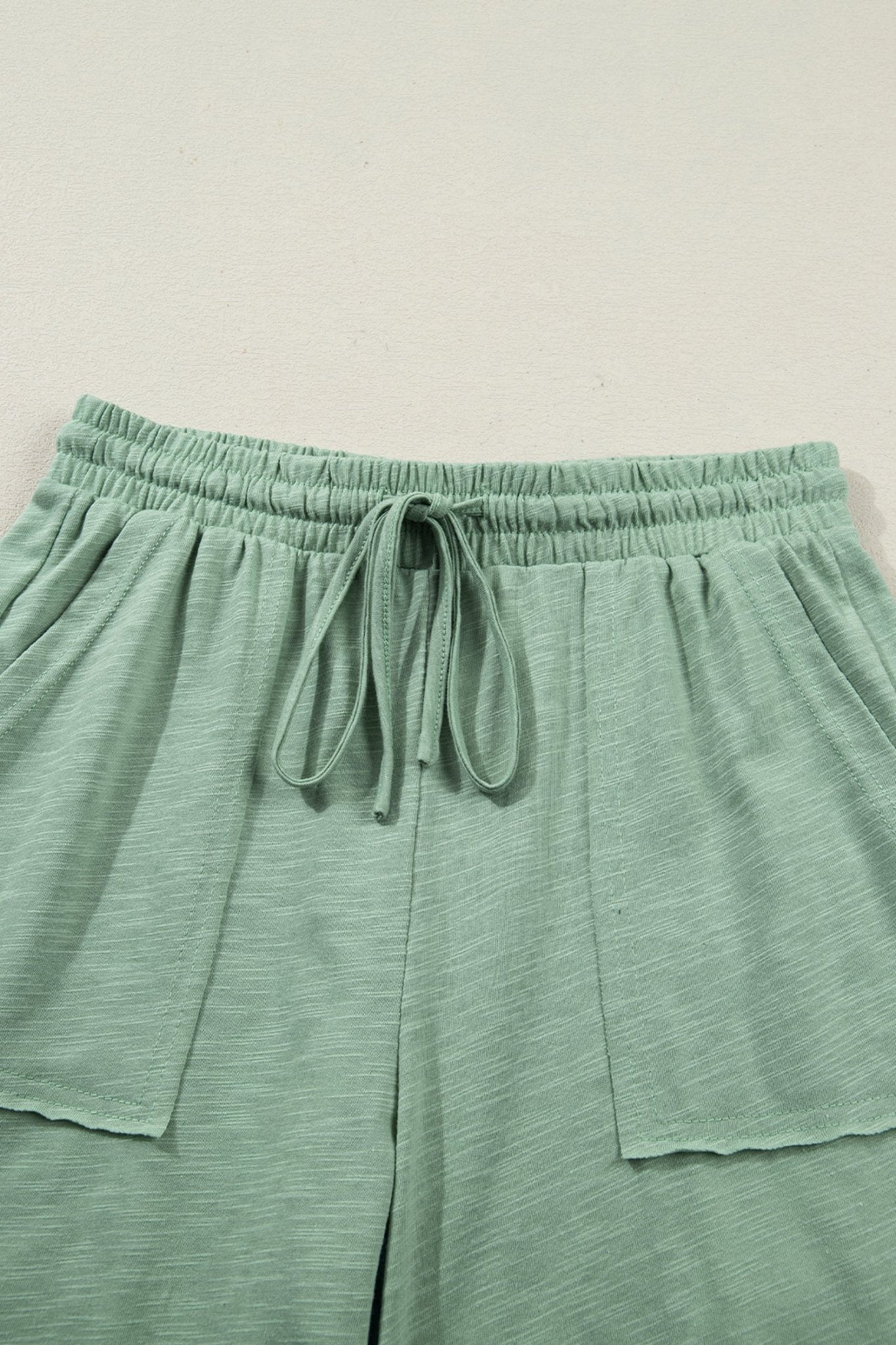 Green lounge pants with drawstring waist on a light beige background