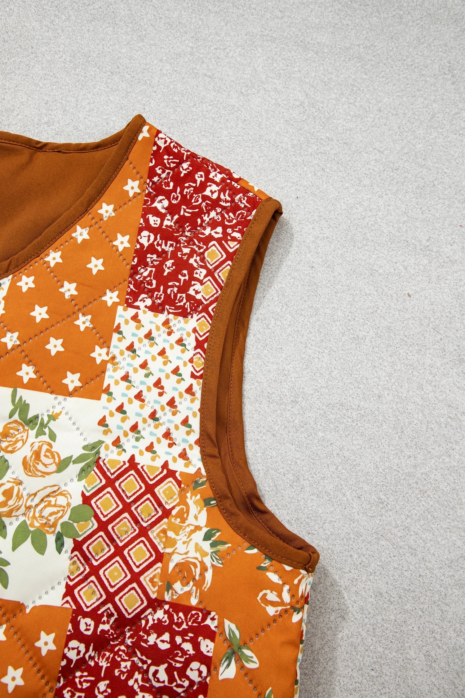 Close-up of sleeveless patchwork quilted vest with orange, red, white patterns and brown ribbed trim.