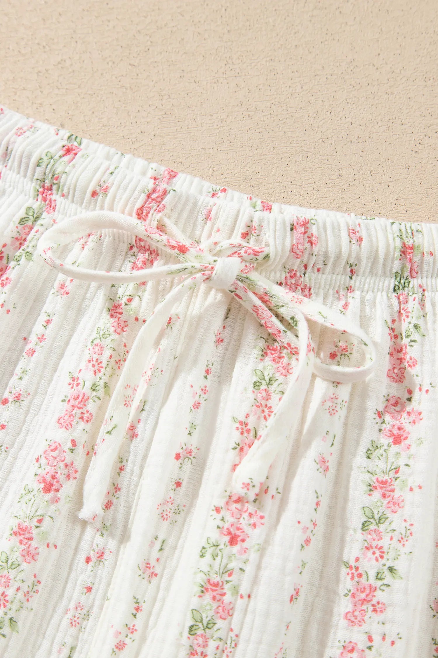Close-up of white gauze garment with pink-green floral print and drawstring bow.