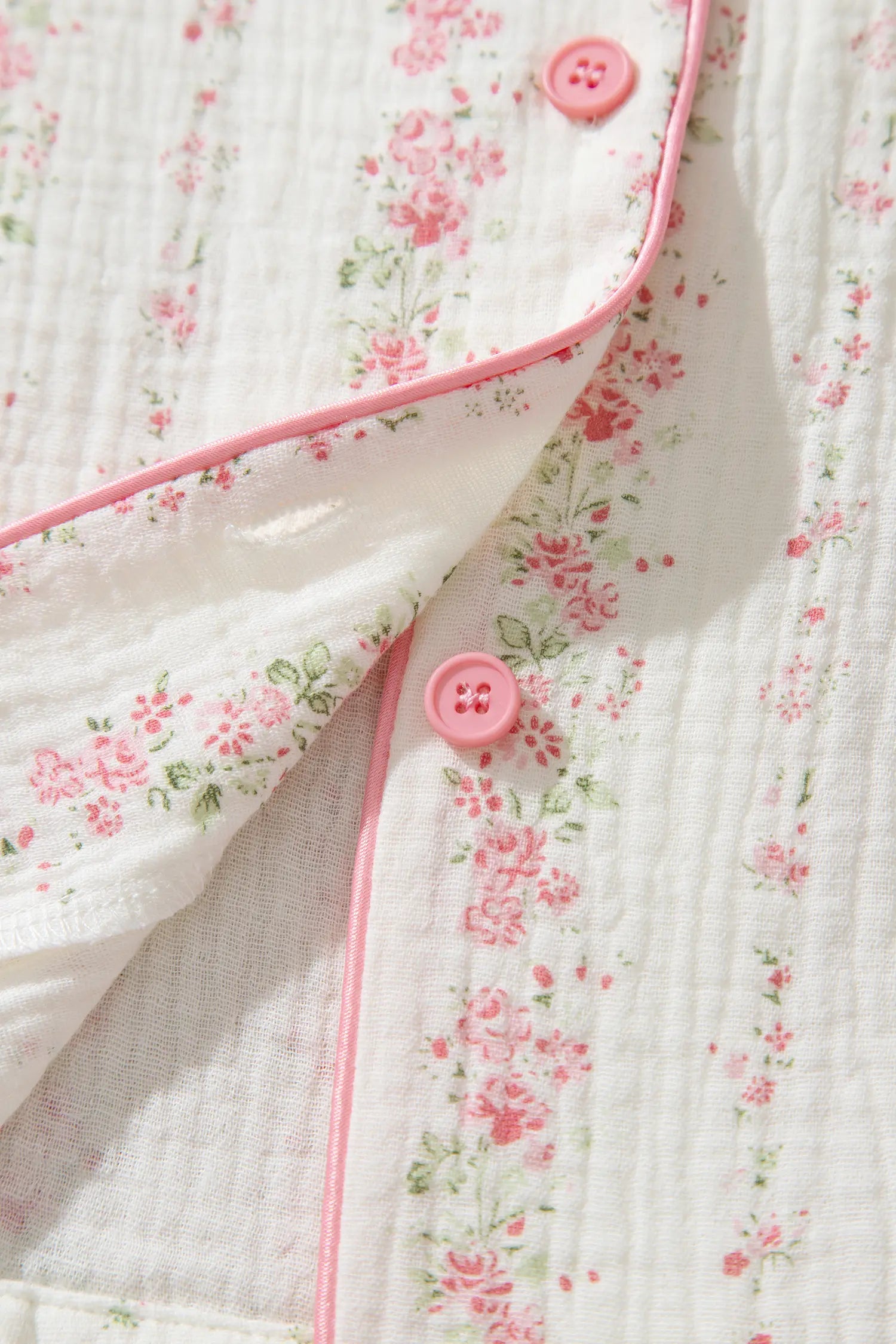 Close-up of a white muslin pajama shirt with a pink and green floral print, pink piping, and pink buttons.