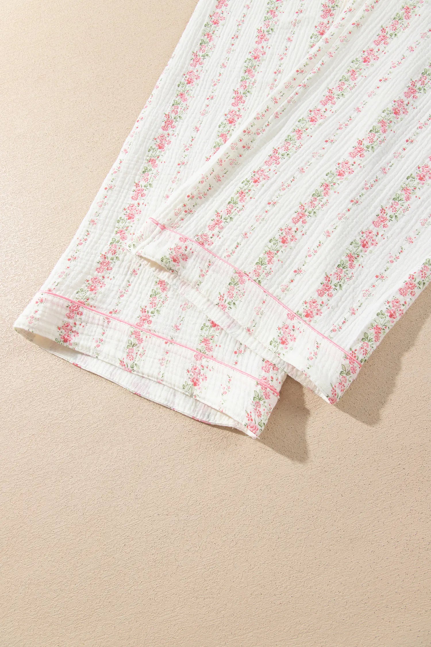 Close-up of white floral fabric with pink piping along the cuff.