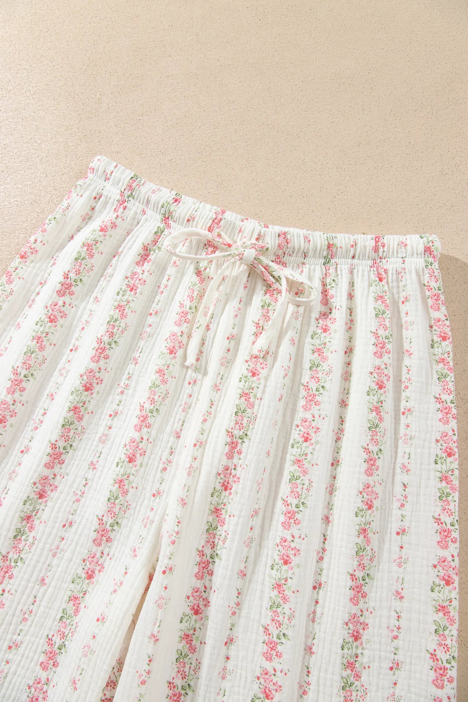 Close-up of white gauze pants with pink-green floral print and drawstring waist.