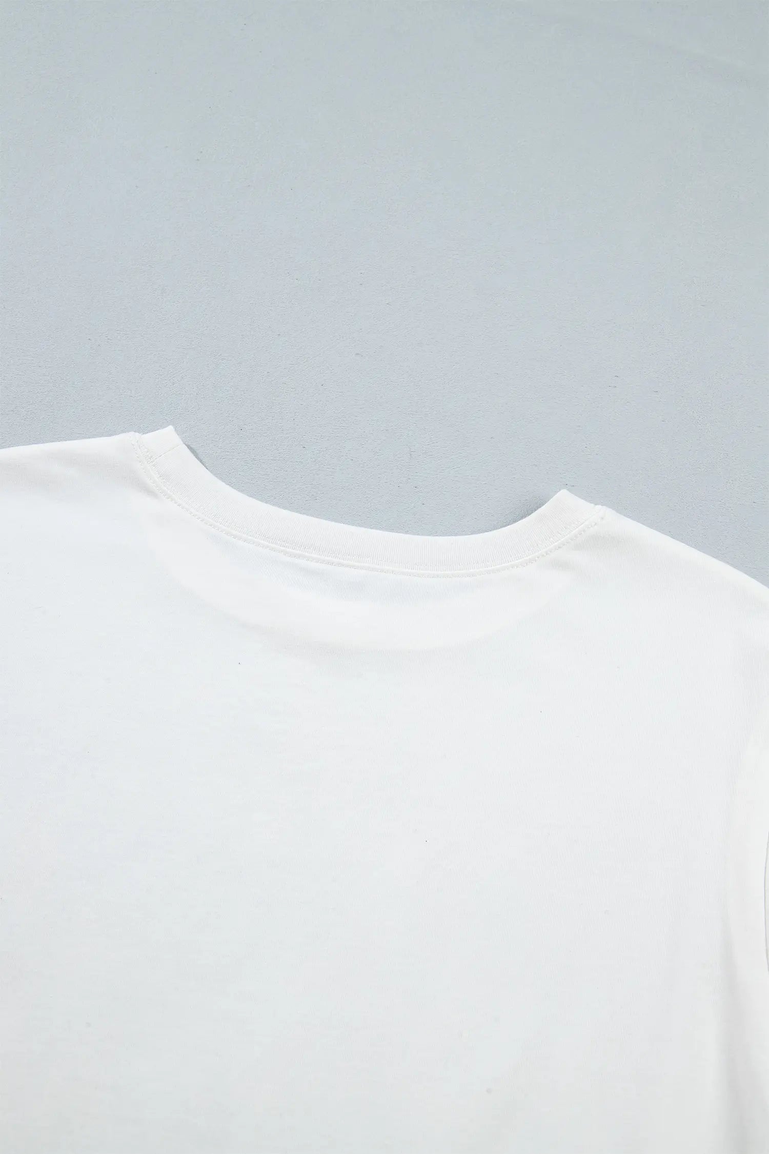 Close-up of a plain white crew-neck t-shirt against a light gray background.