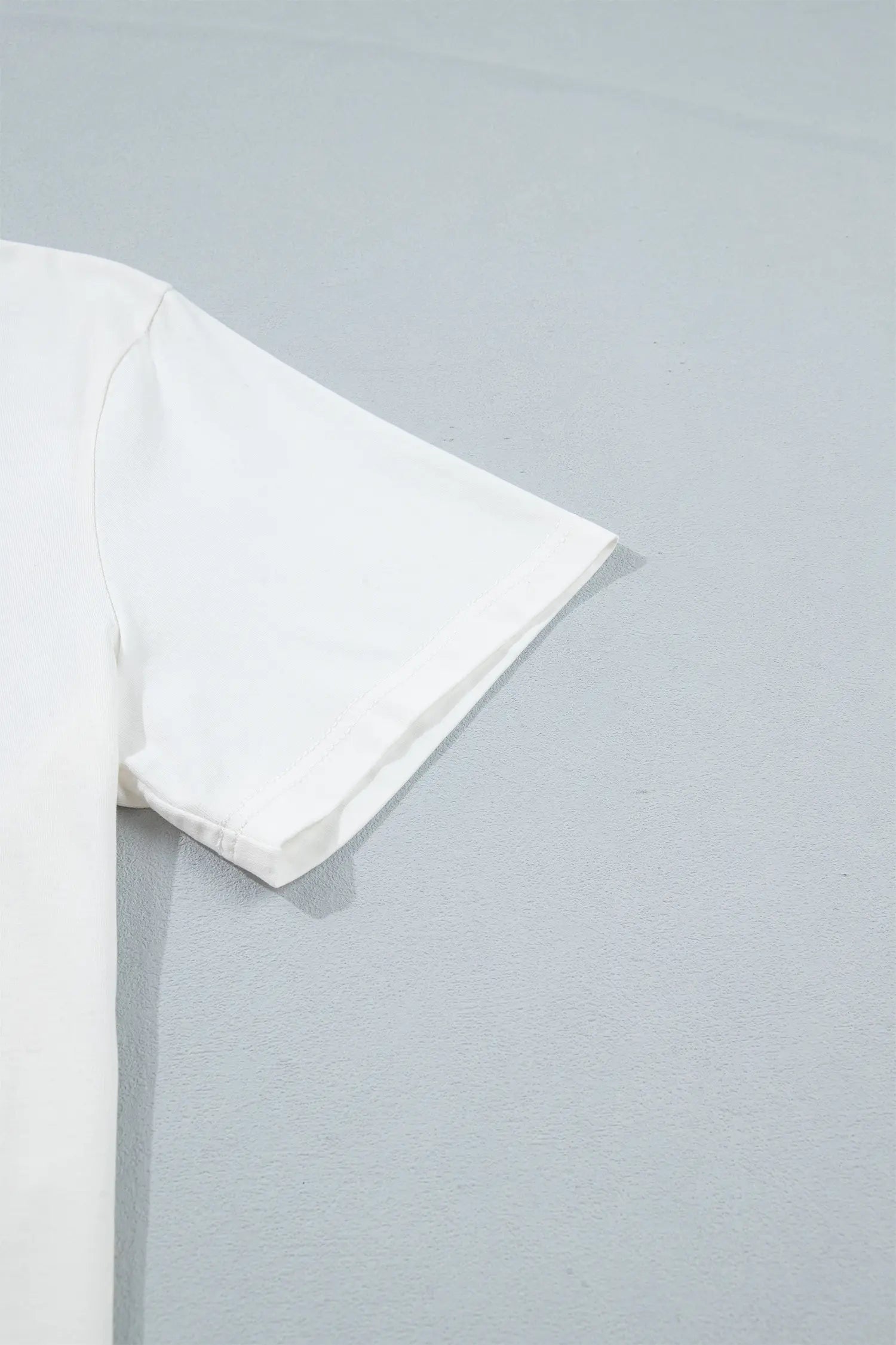 A close-up of a white short-sleeve t-shirt sleeve laid flat on a light gray textured surface.