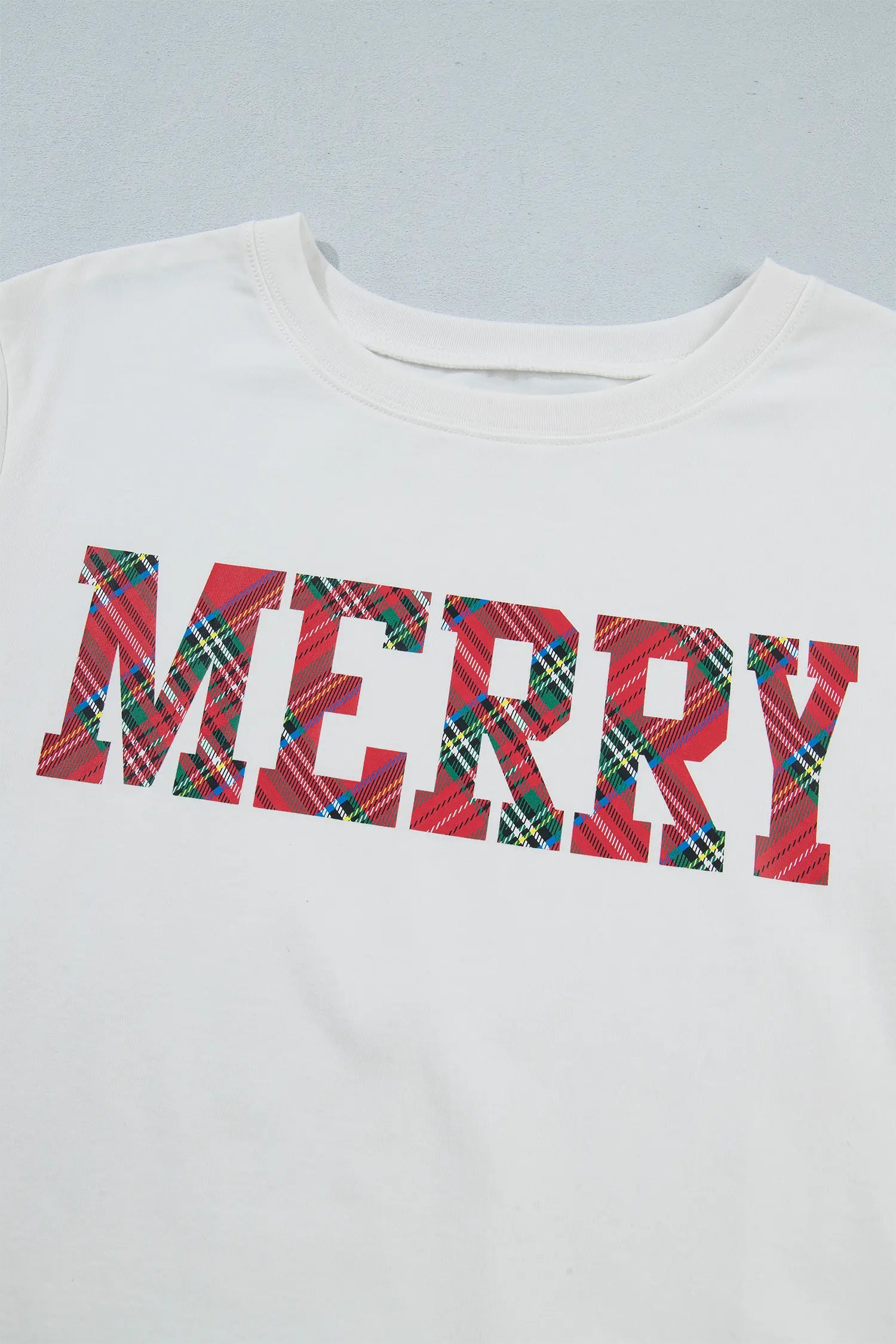 Close-up of white crewneck tee with MERRY in red, green, blue plaid.