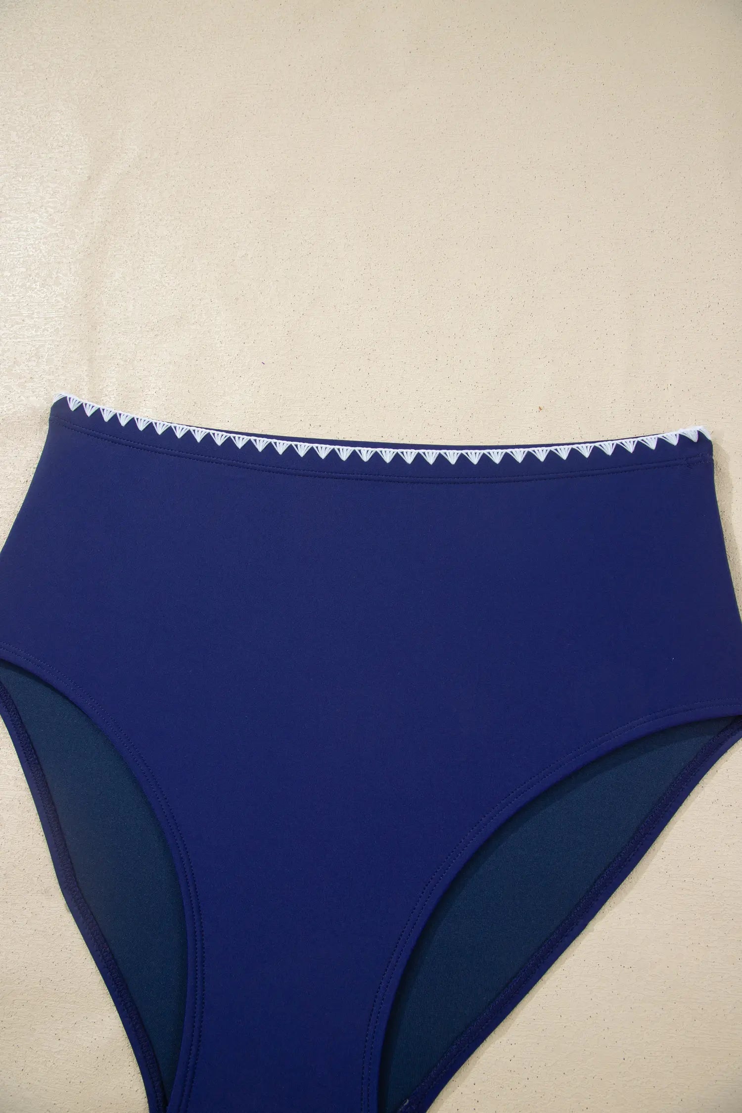 Blue bikini bottom with white trim on a beige surface