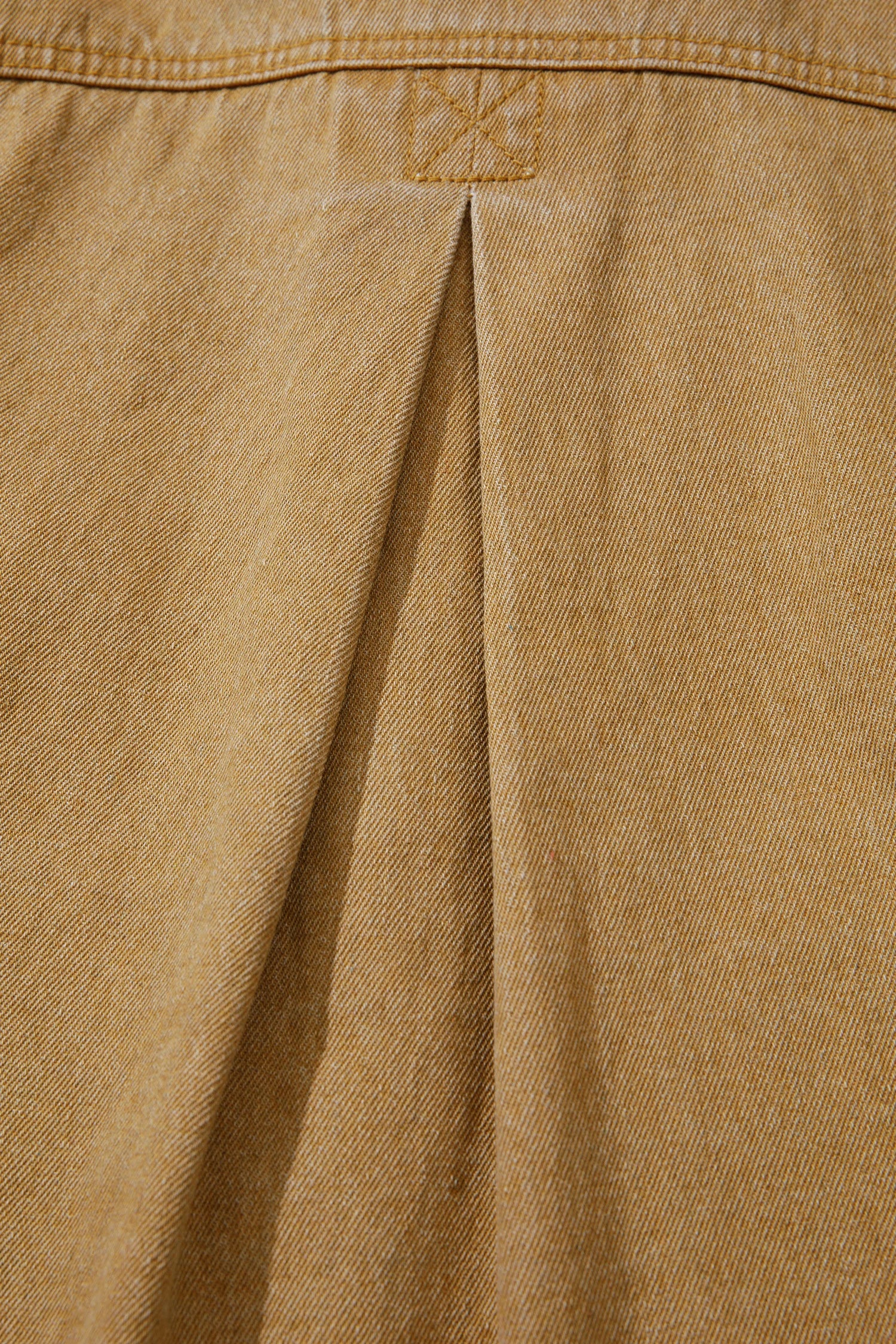 Close-up of a tan or camel-colored fabric garment showing a vertical pleat and stitched detail near the top.