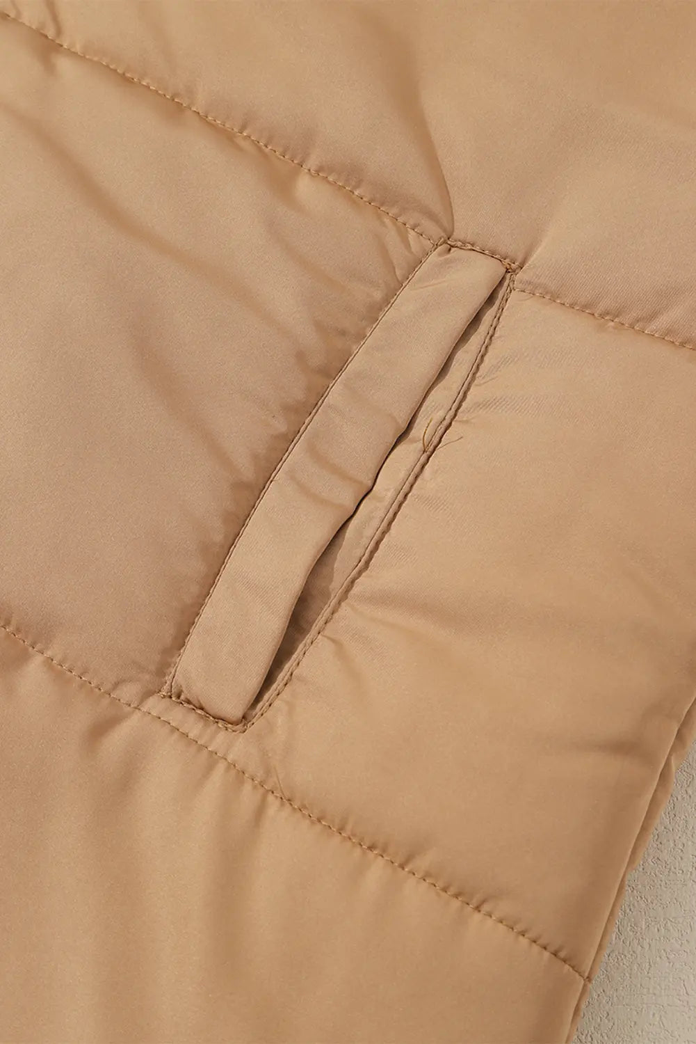 Close-up of warm tan quilted puffer jacket showing stitched pocket detail and textured fabric.