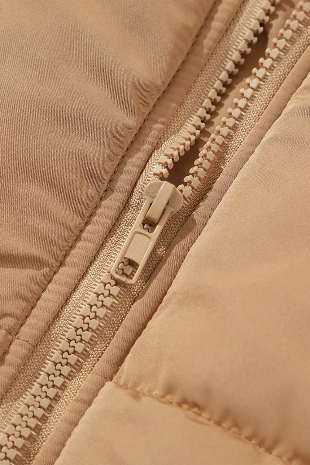 Close-up of warm beige quilted puffer jacket with textured fabric and matching beige zipper pull.