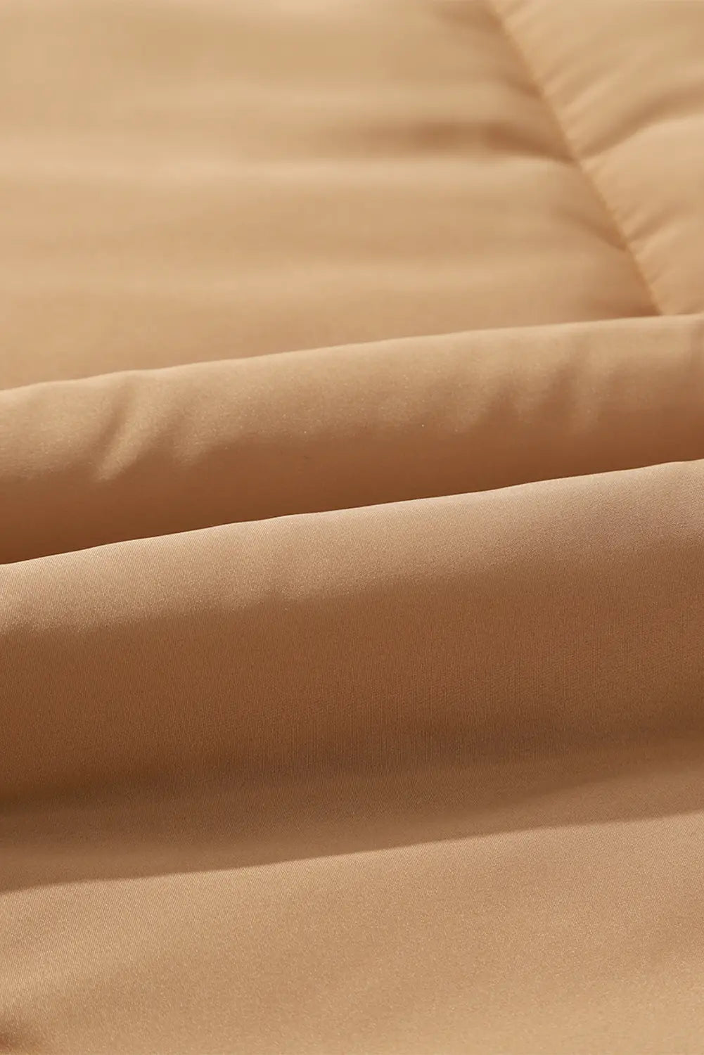 A close-up of soft peach-beige fabric with gentle folds and a smooth texture.