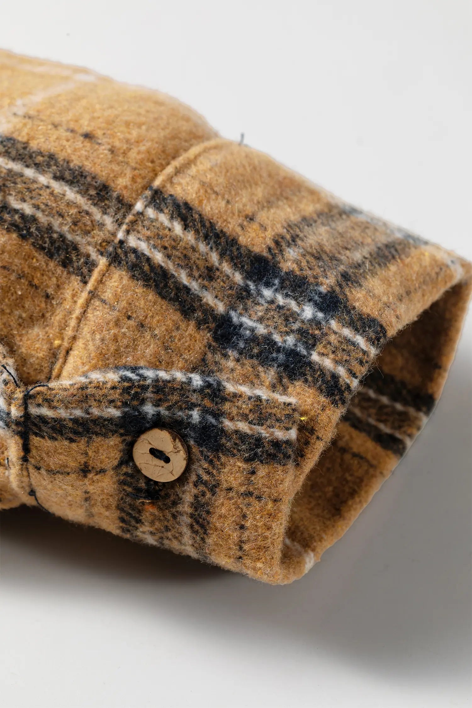 Close-up of a plaid wool or flannel shirt cuff in tan, brown, and black with a visible wooden button.