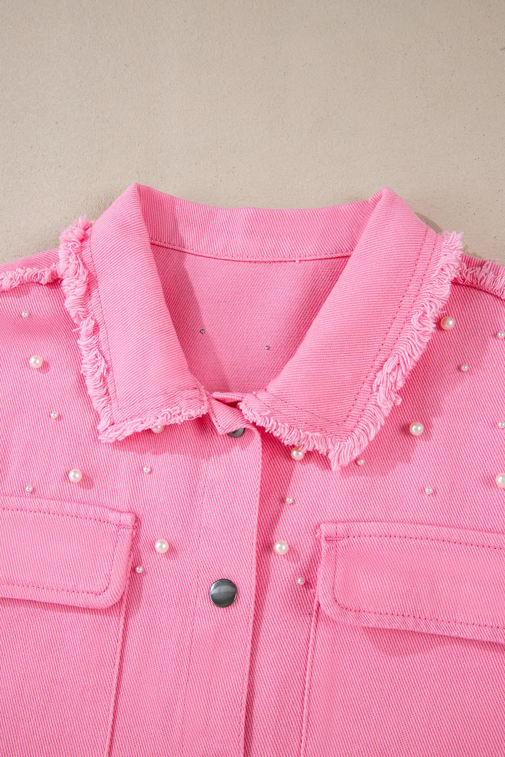 Pink shirt with pearl embellishments on a beige background