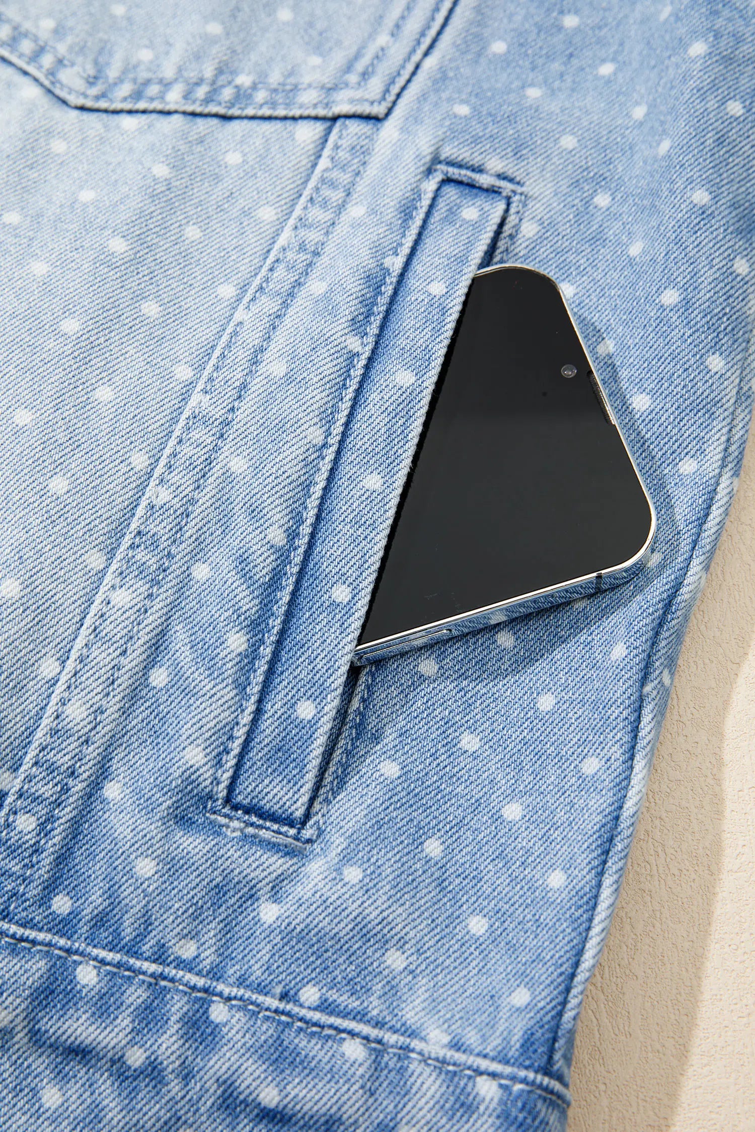 Close-up of light blue polka-dot denim jacket with a black smartphone partially tucked into the side pocket.