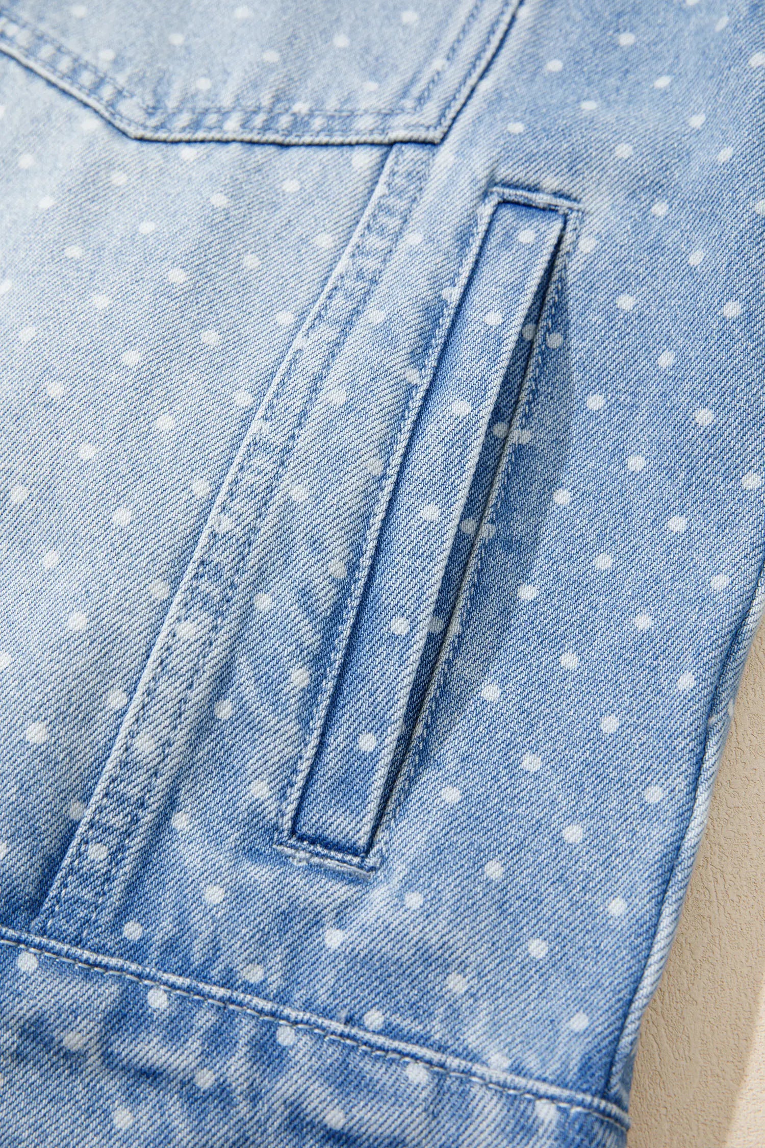 Close-up of a light blue denim garment with a white polka dot pattern and a vertical welt pocket.