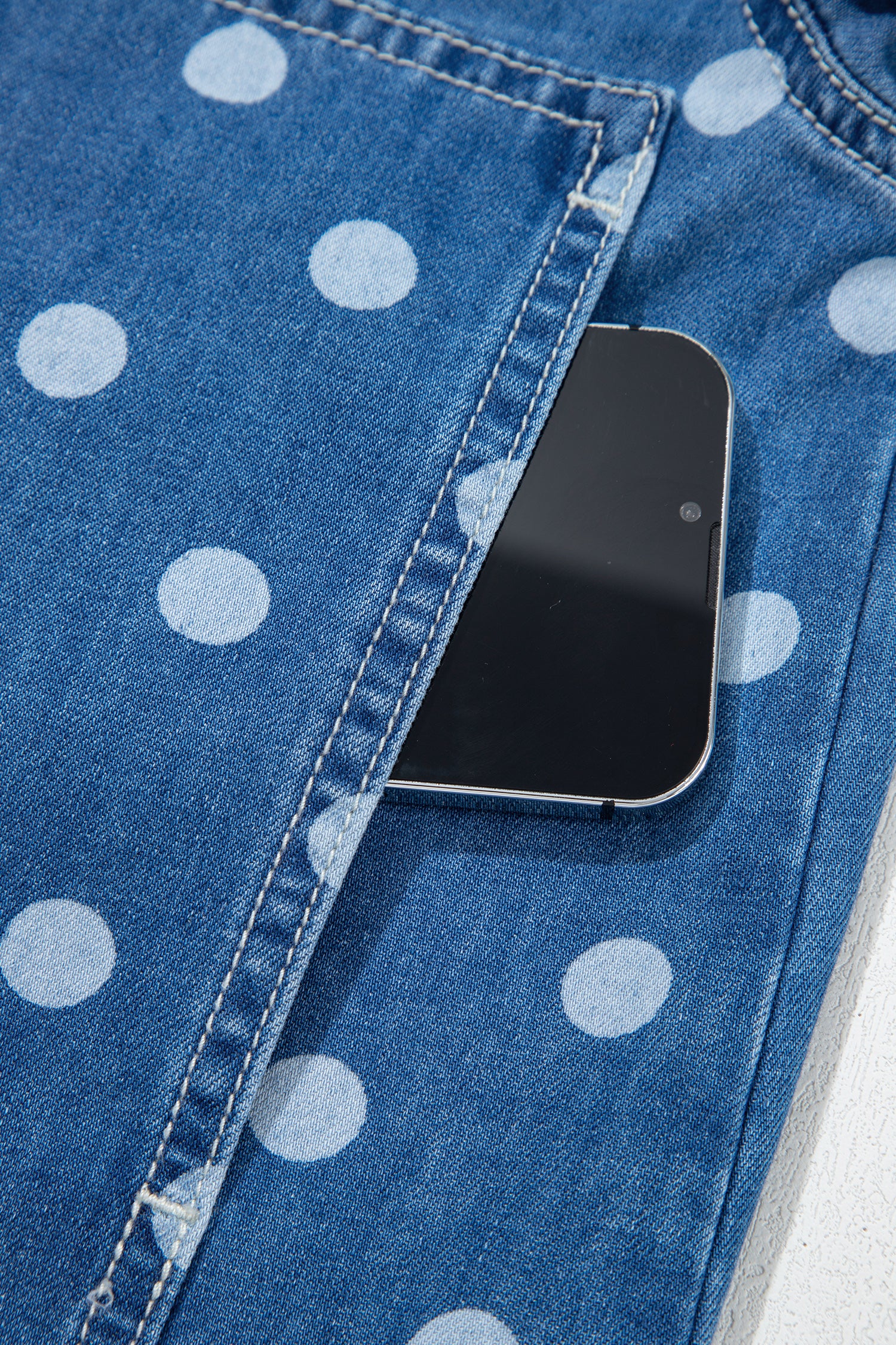 Close-up of blue denim jeans with large white polka dots and a black smartphone in the back pocket.