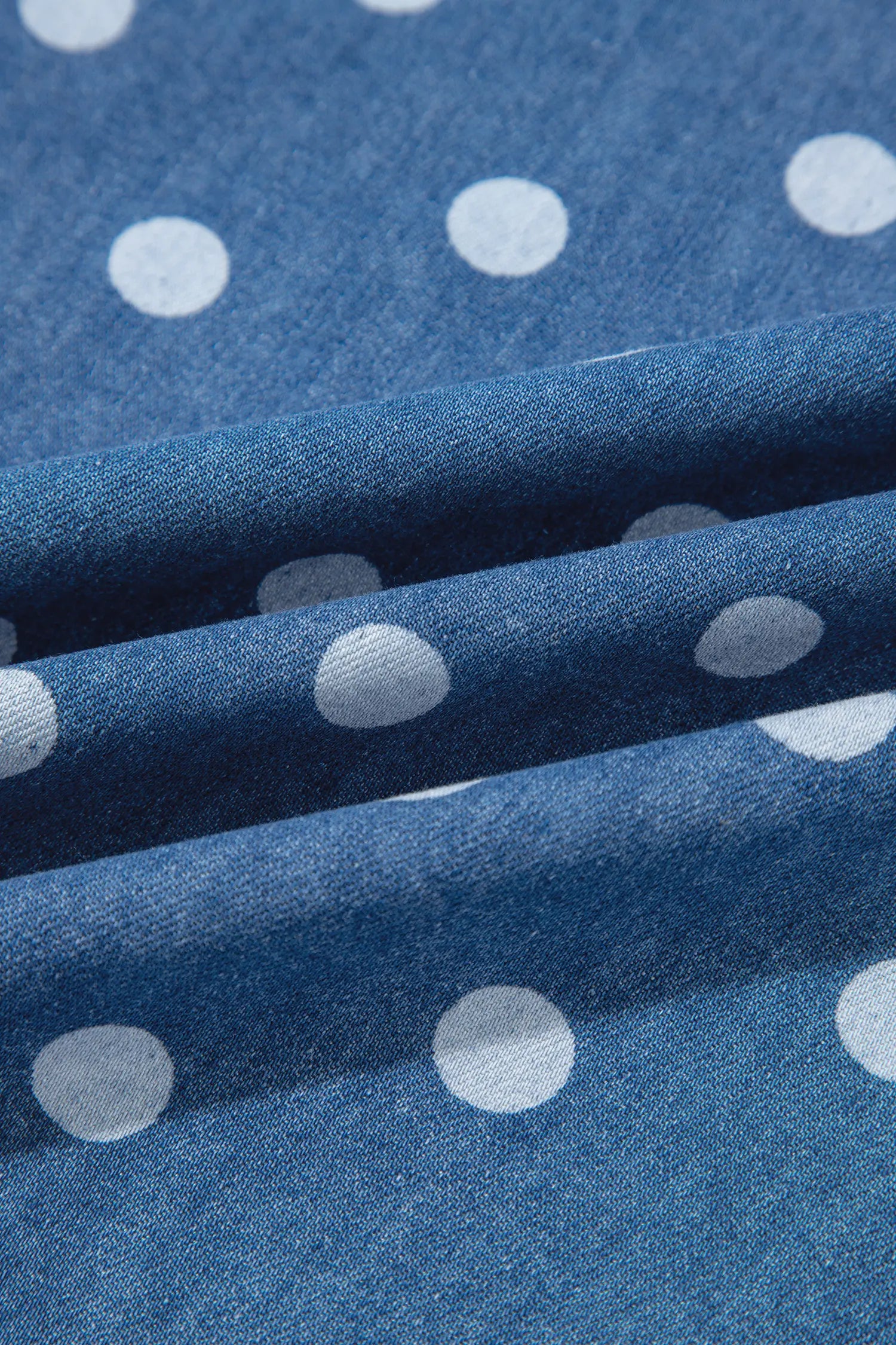 A close-up of blue fabric with a white polka dot pattern, draped in soft folds to show the texture and pattern repeat.