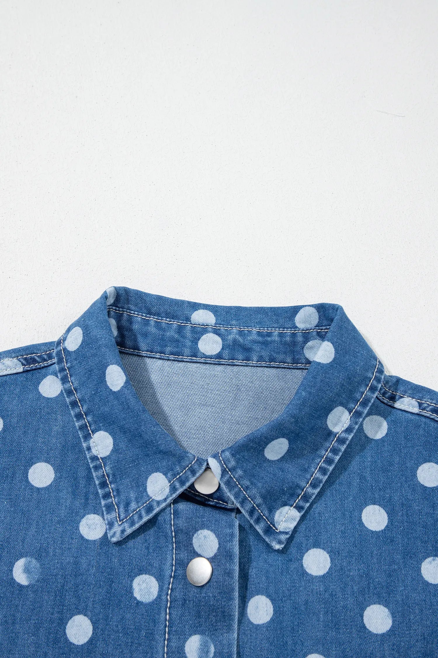 Close-up of blue denim shirt with white polka dots, showing collar and front button details.