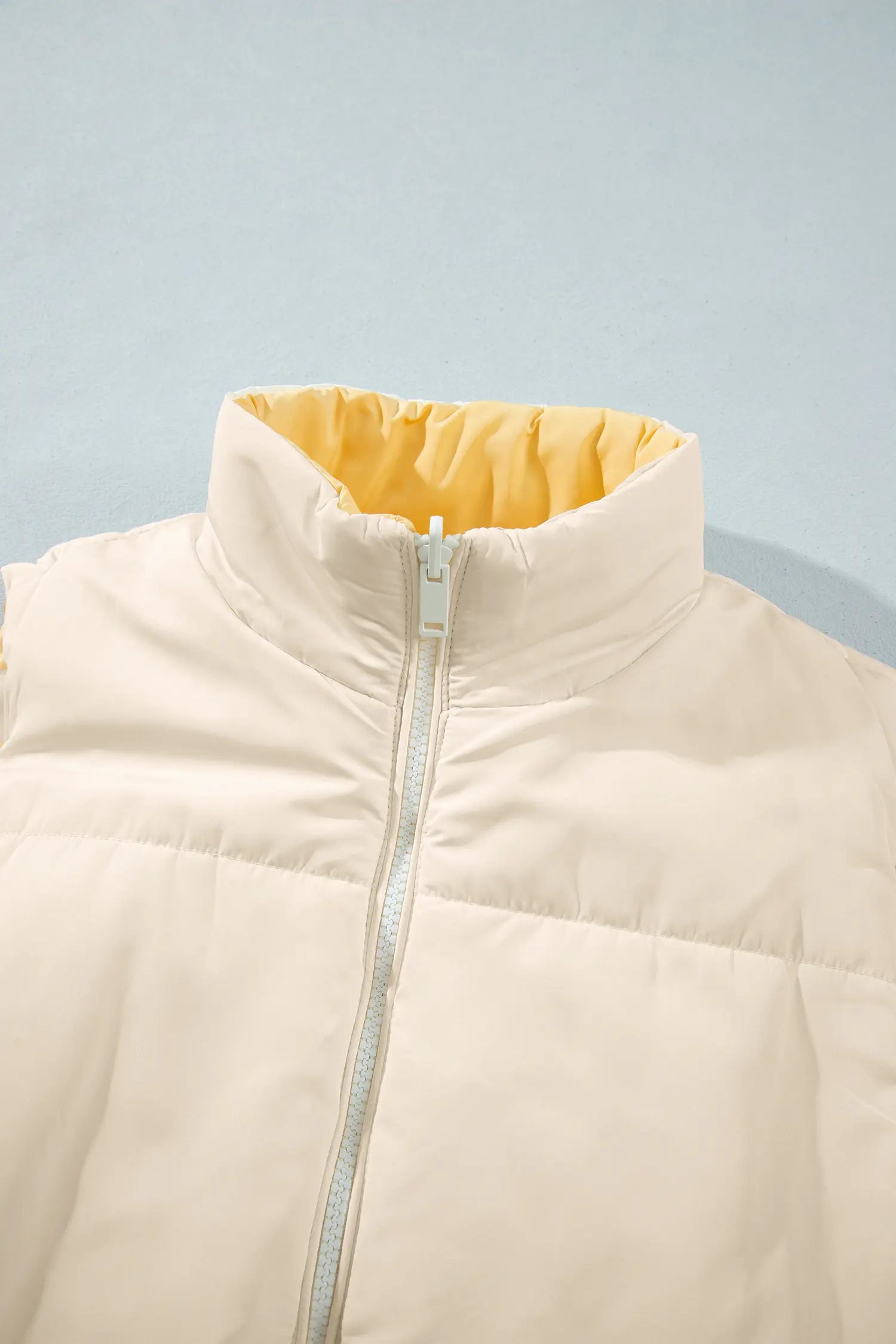 Close-up of cream puffer jacket with bright yellow collar lining and light blue zipper.