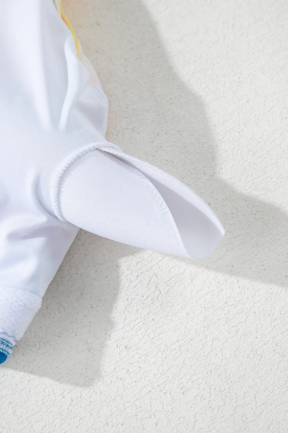 Close-up of a white garment with ruffled details on a textured beige surface
