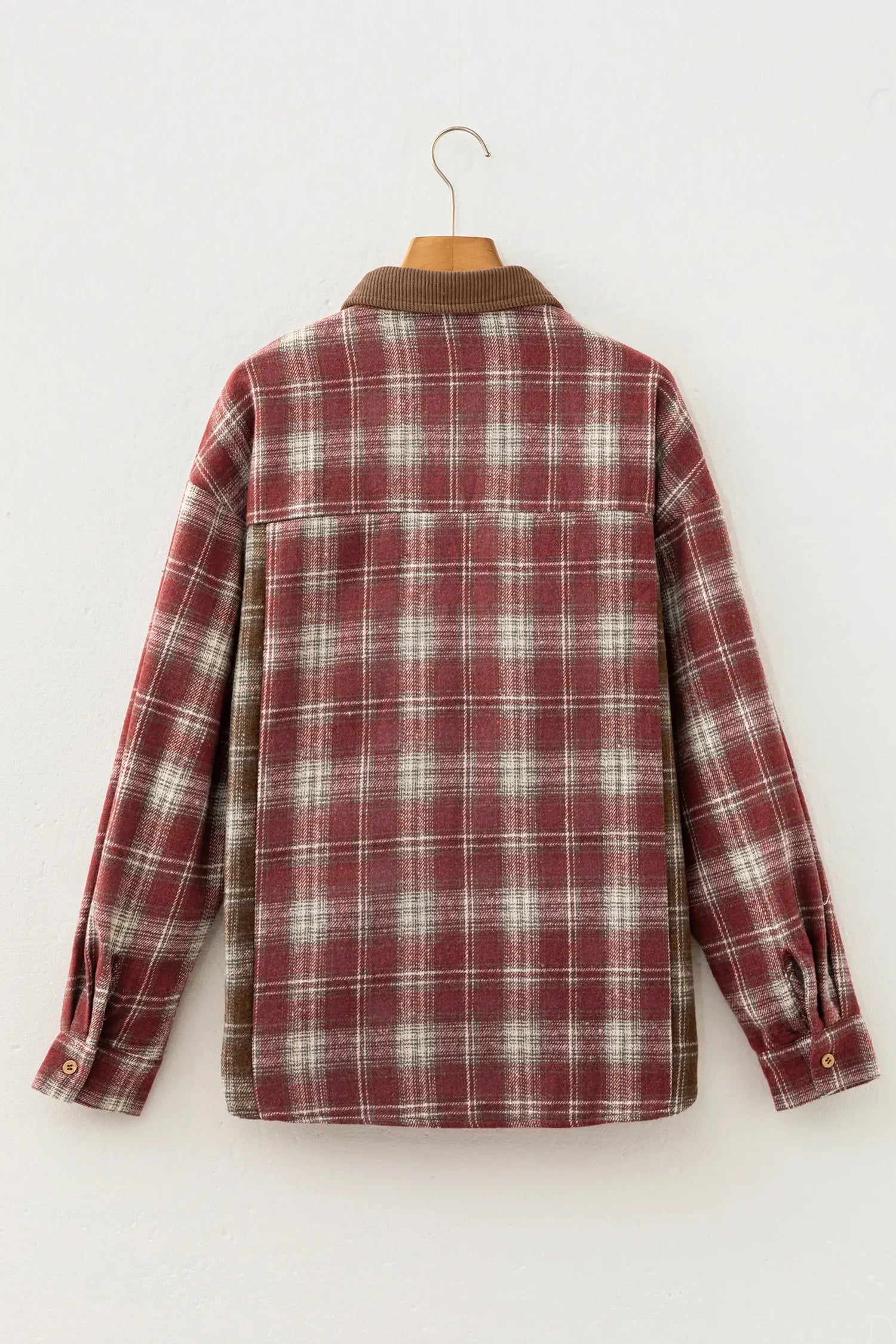 A red and white plaid long-sleeve flannel shirt jacket hanging on a wooden hanger against a plain white wall.