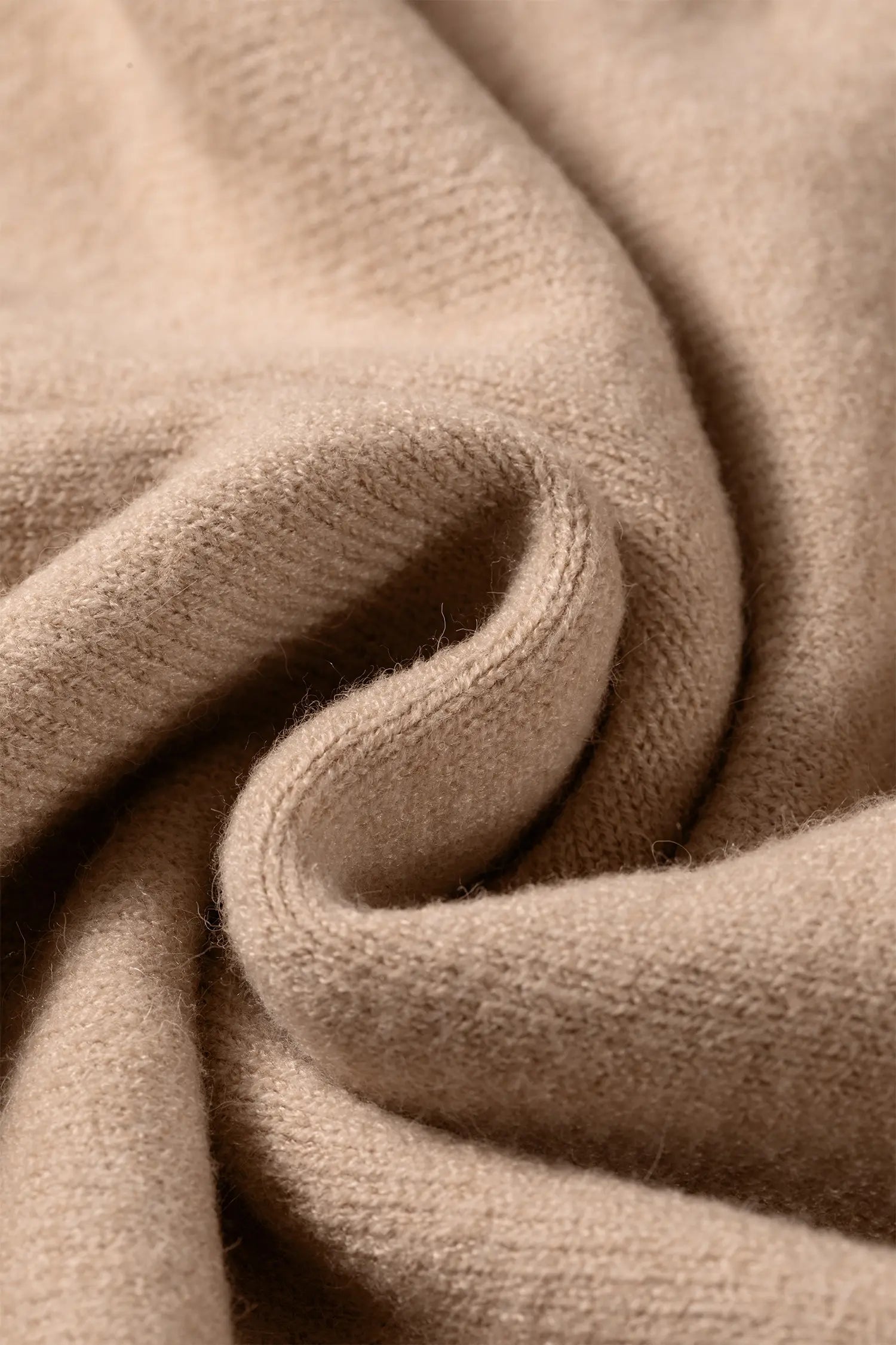 A close-up of draped beige knit fabric with soft folds and a smooth, slightly lustrous texture.