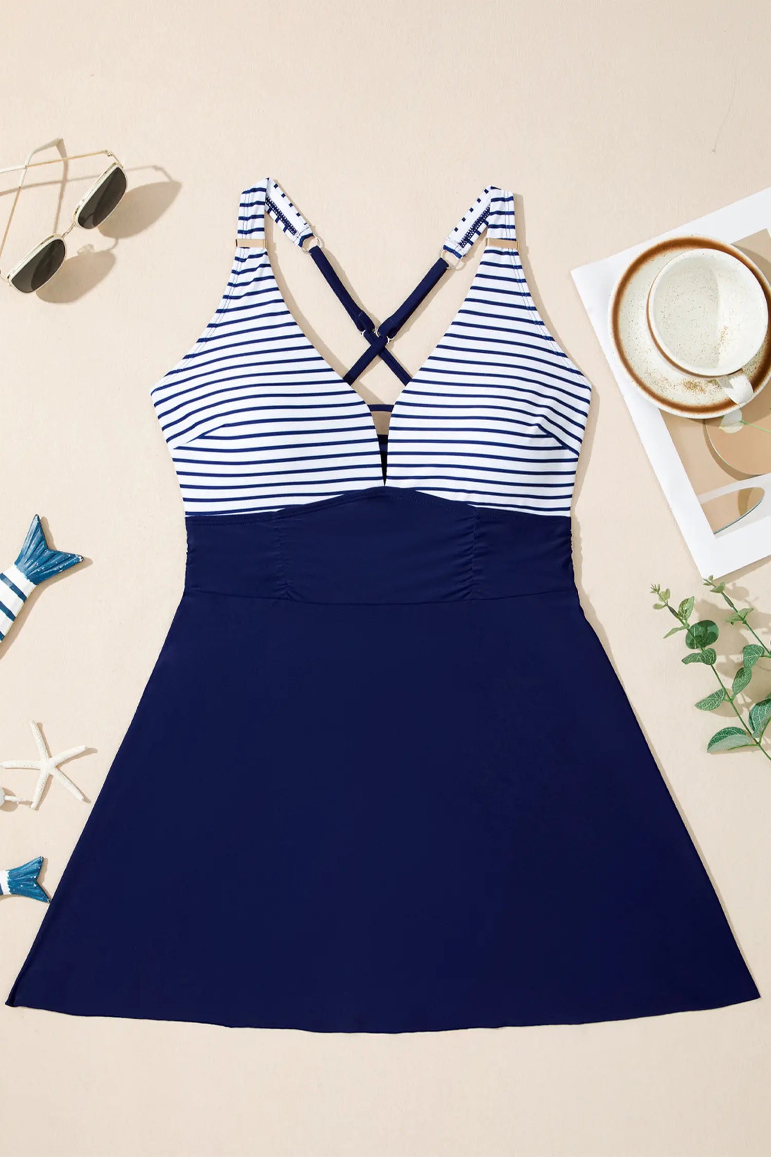 Navy and white striped swimsuit on a beige surface with sunglasses and a cup.