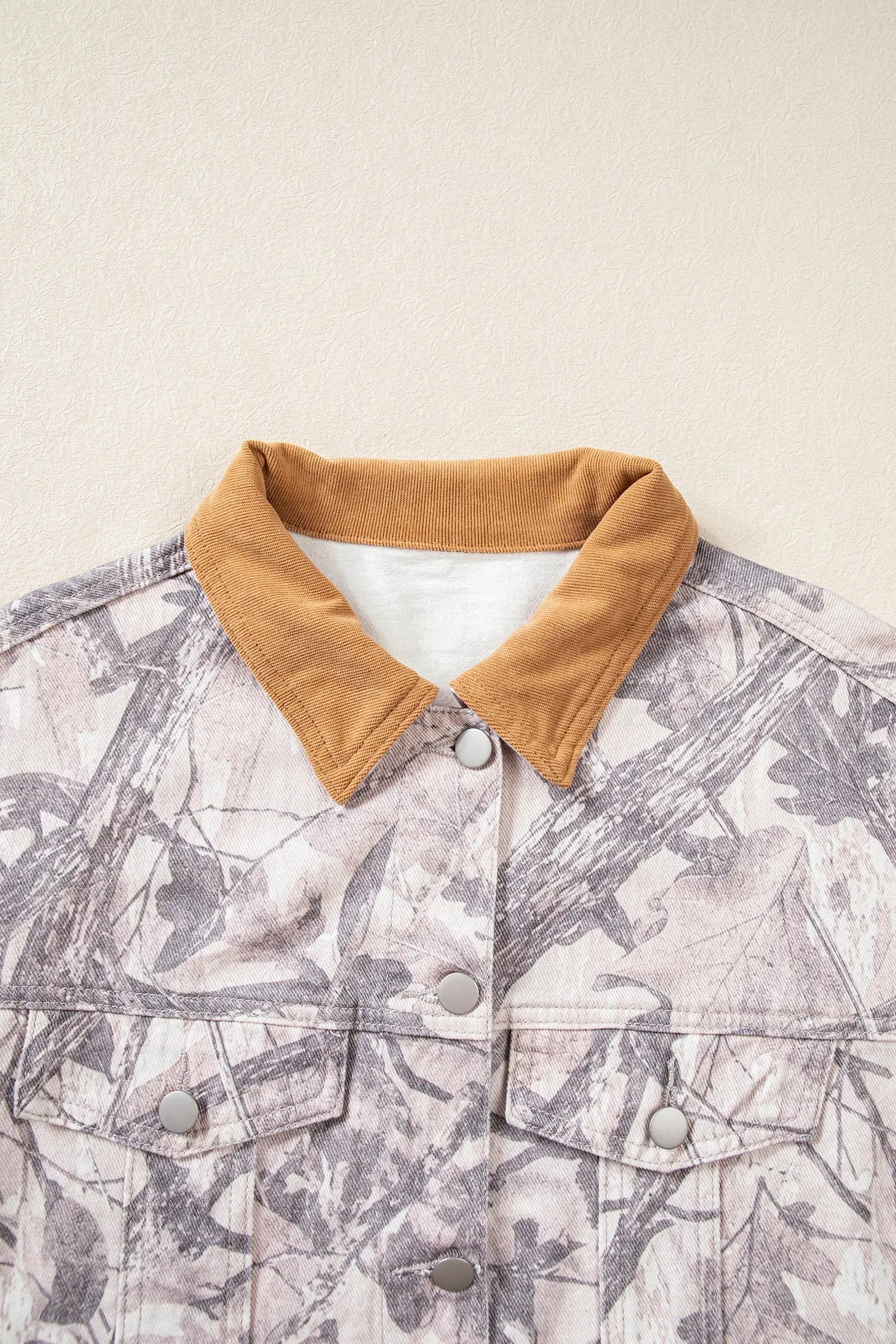 Close-up of gray and white camouflage jacket with a contrasting tan corduroy collar against a beige background.