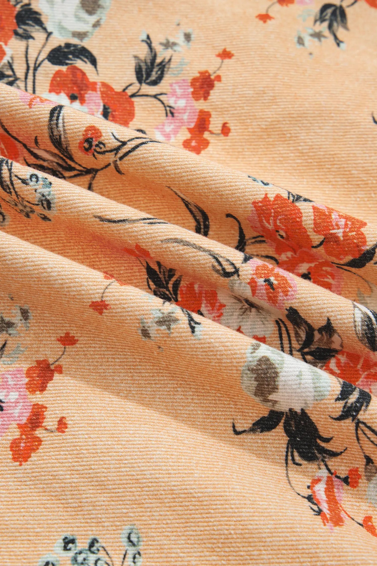 A close-up of draped peach-colored fabric with a floral print featuring orange, pink, black, and white flowers.