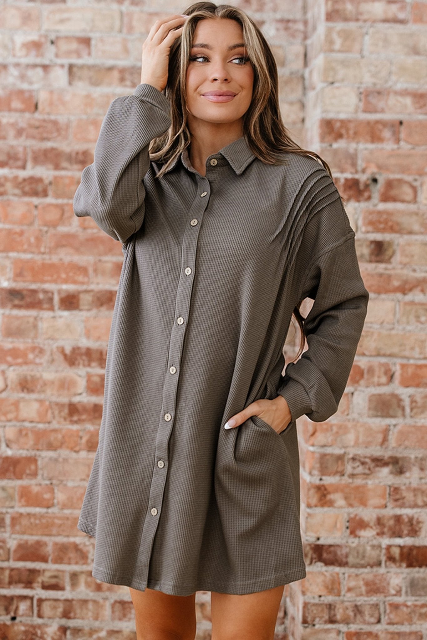 Woman wearing a gray shirt dress against a brick wall