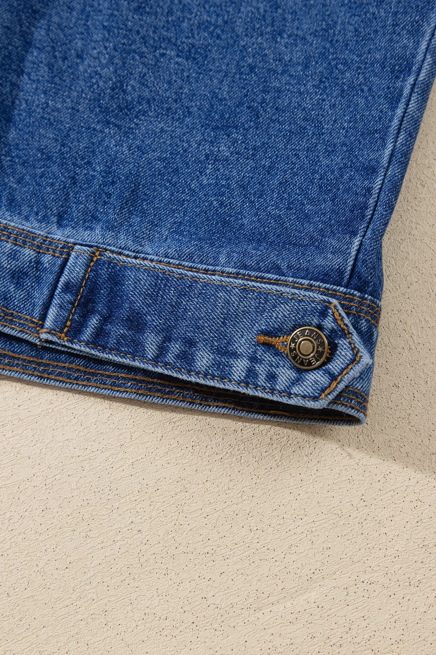 Close-up of blue denim garment with folded cuff, brass button