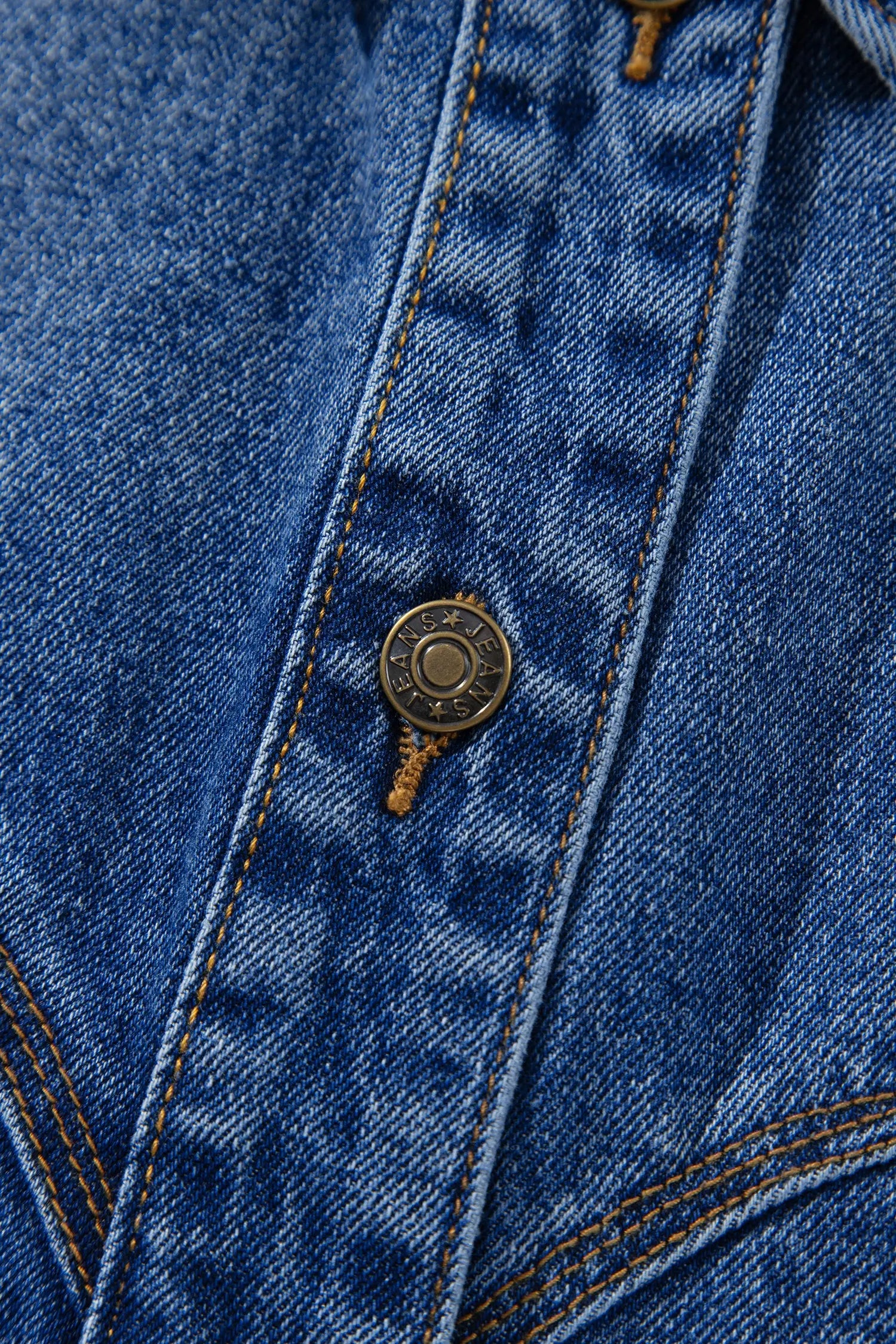 Close-up of a blue denim jacket showing the button closure, contrast stitching